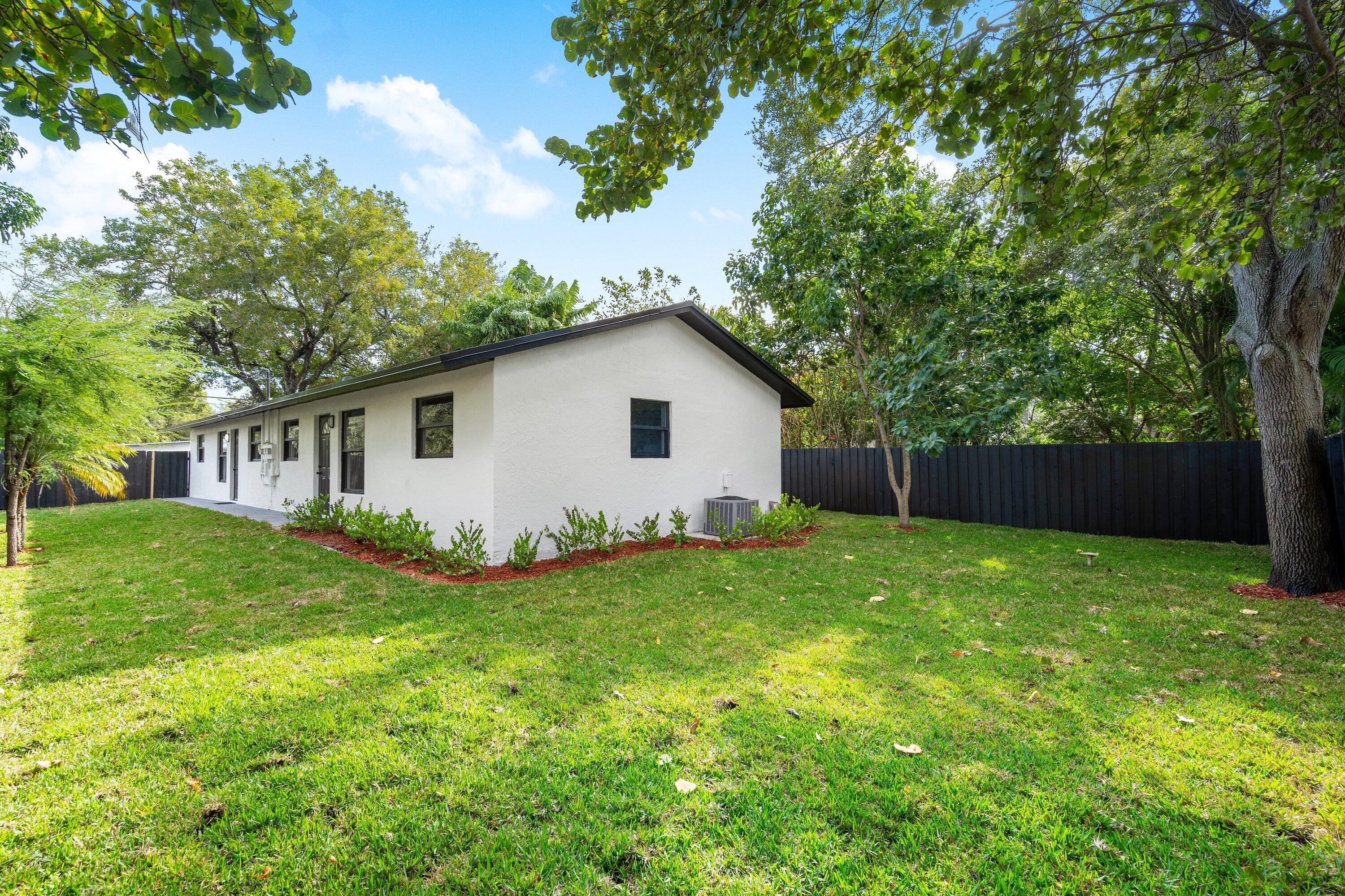 Rear exterior featuring white stucco siding, dark trim, manicured lawn, and black perimeter fencing