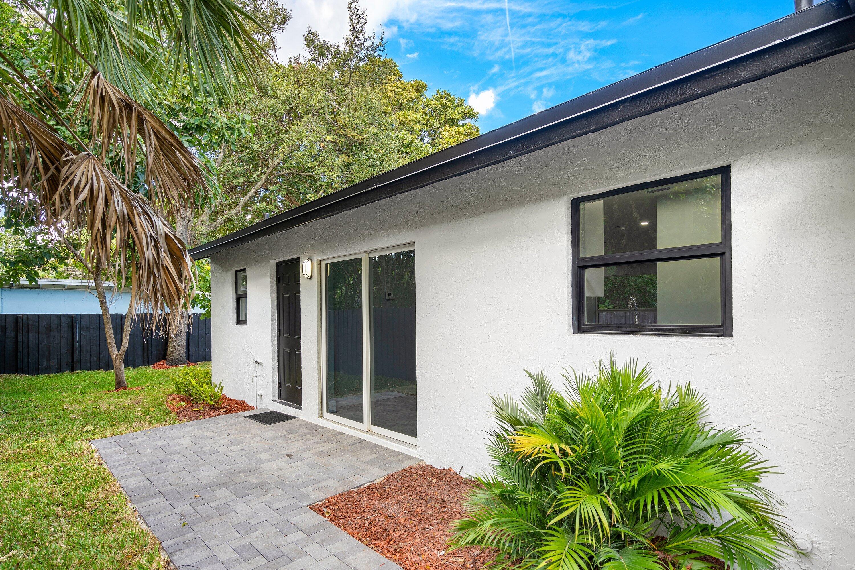 Stucco exterior featuring sliding glass doors, a paver patio, dark-finished window frames, and exterior wall-mounted lighting