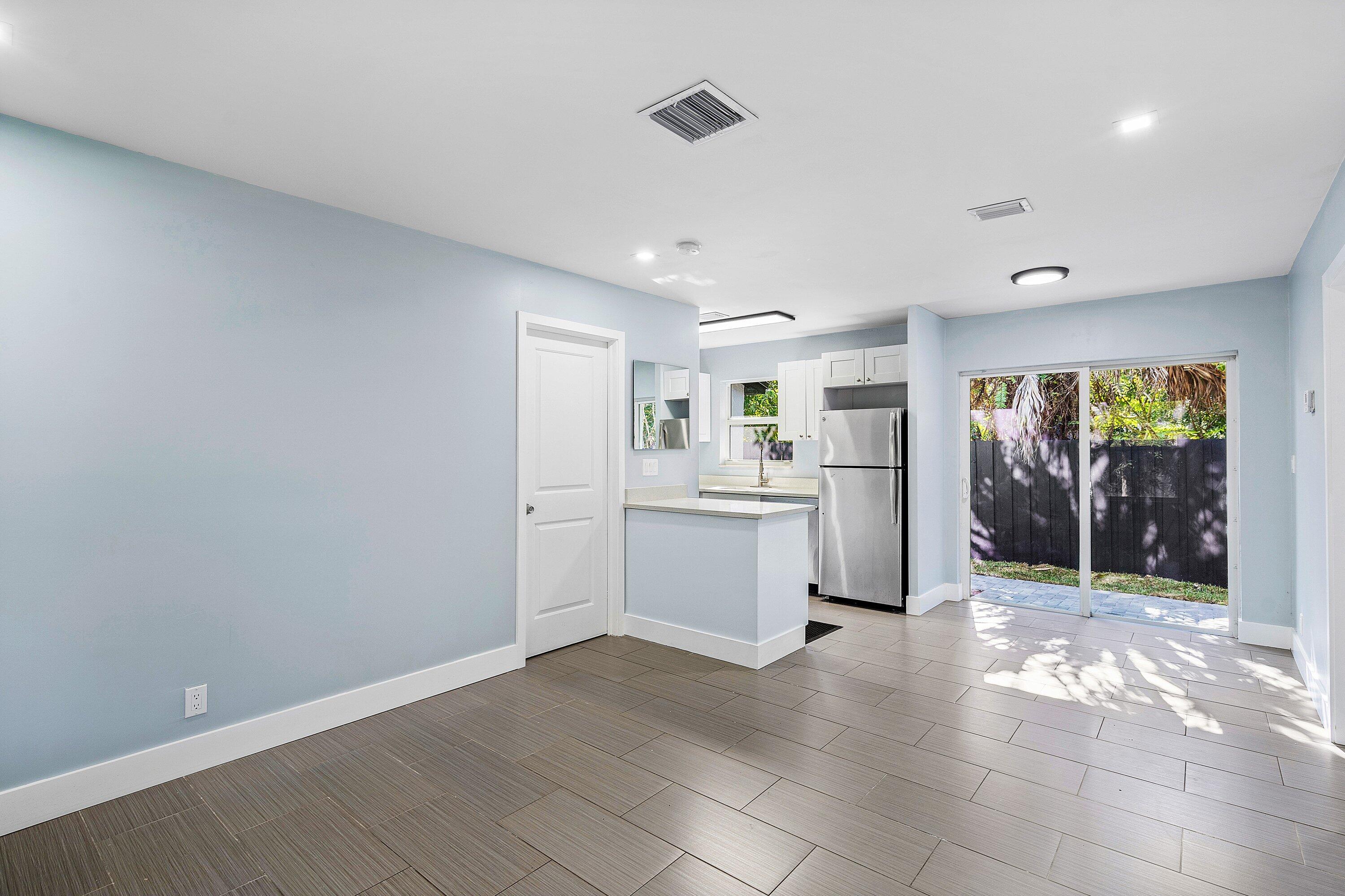 Open-concept interior featuring large-format tile flooring, kitchen with stainless steel refrigerator, white cabinetry, solid-surface countertops, and sliding glass doors