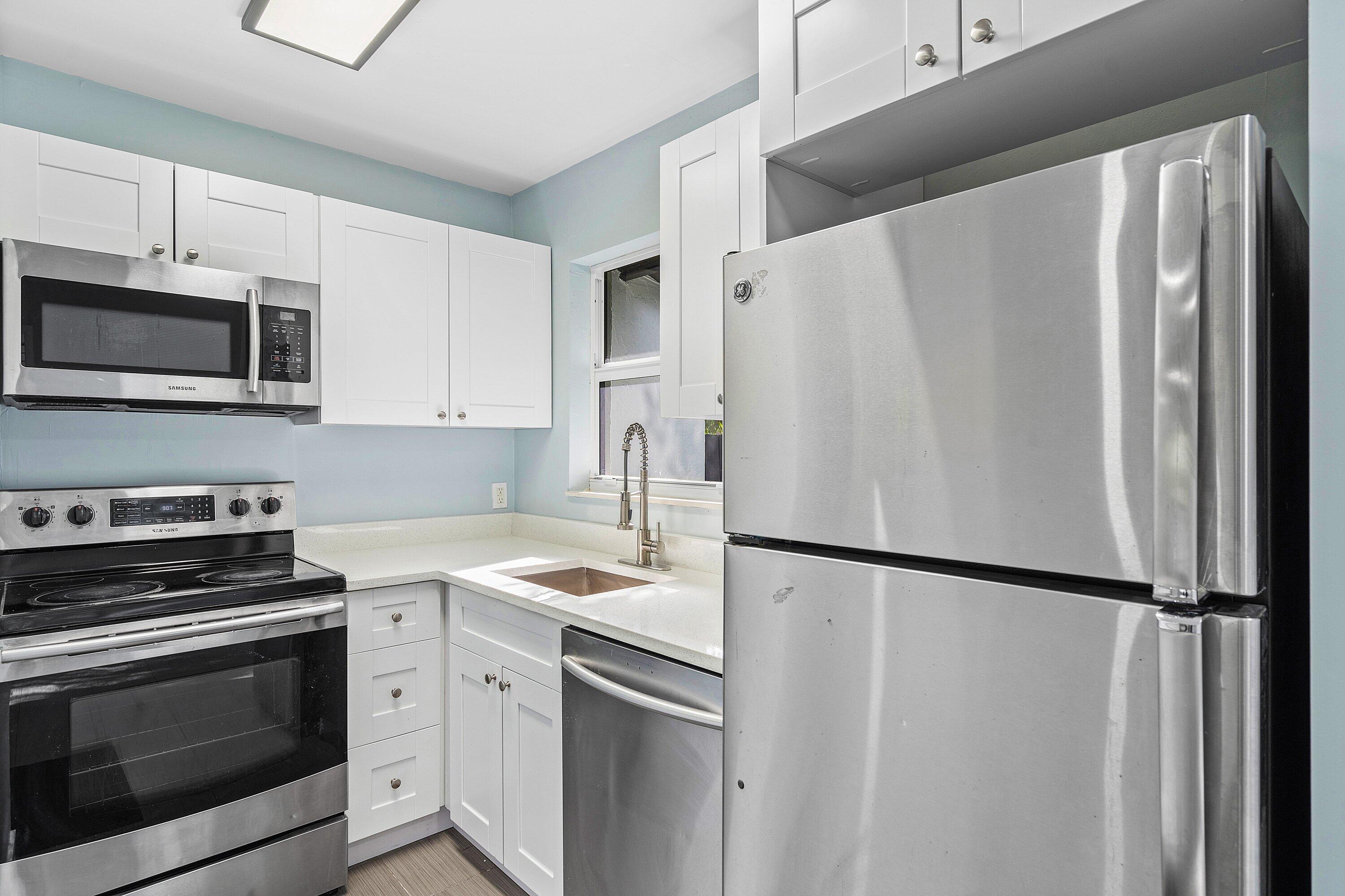 Kitchen featuring white shaker-style cabinetry, solid-surface countertops, stainless steel appliances, and a gooseneck faucet