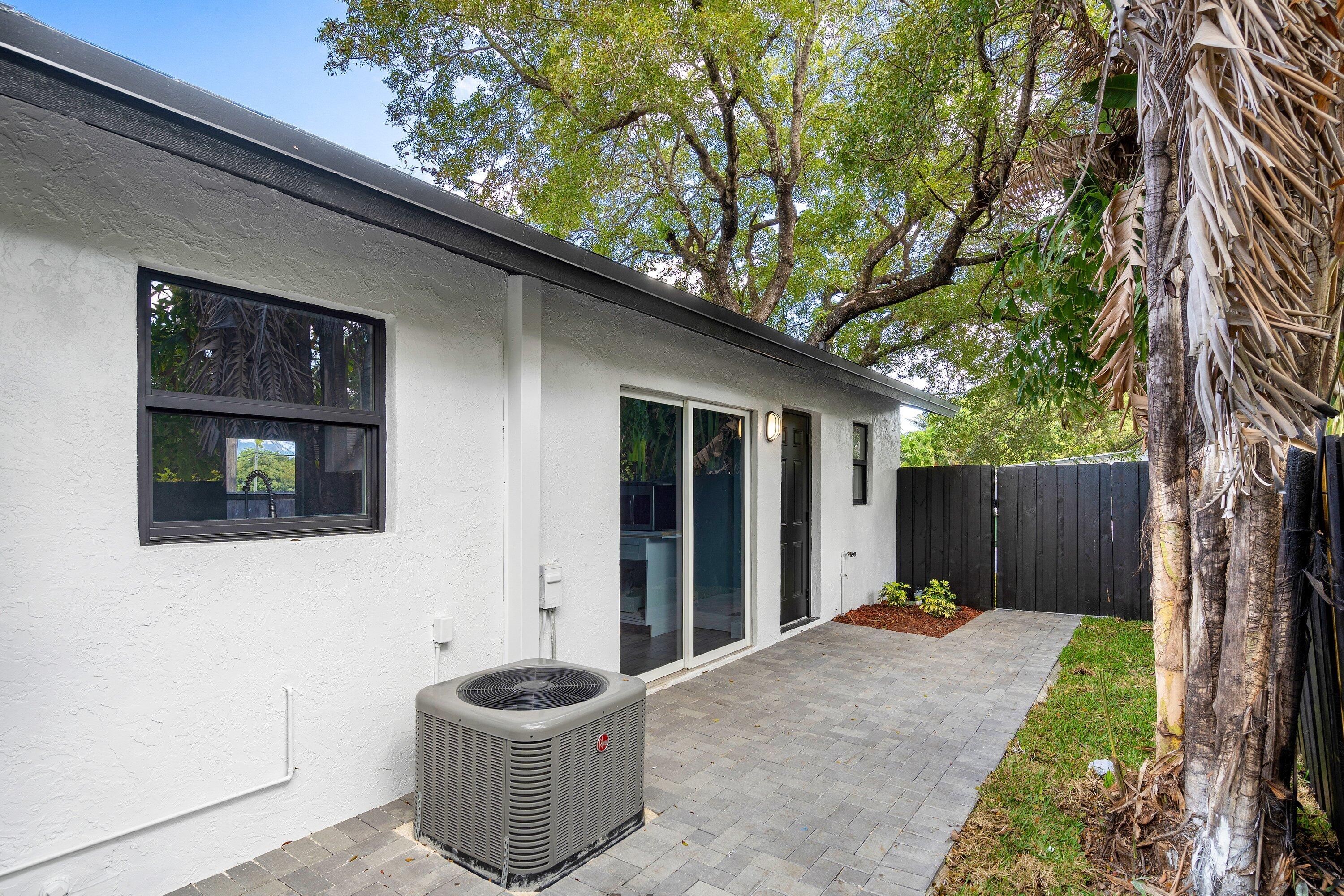Stucco exterior featuring sliding glass doors, paver patio, and dark wood-tone privacy fencing
