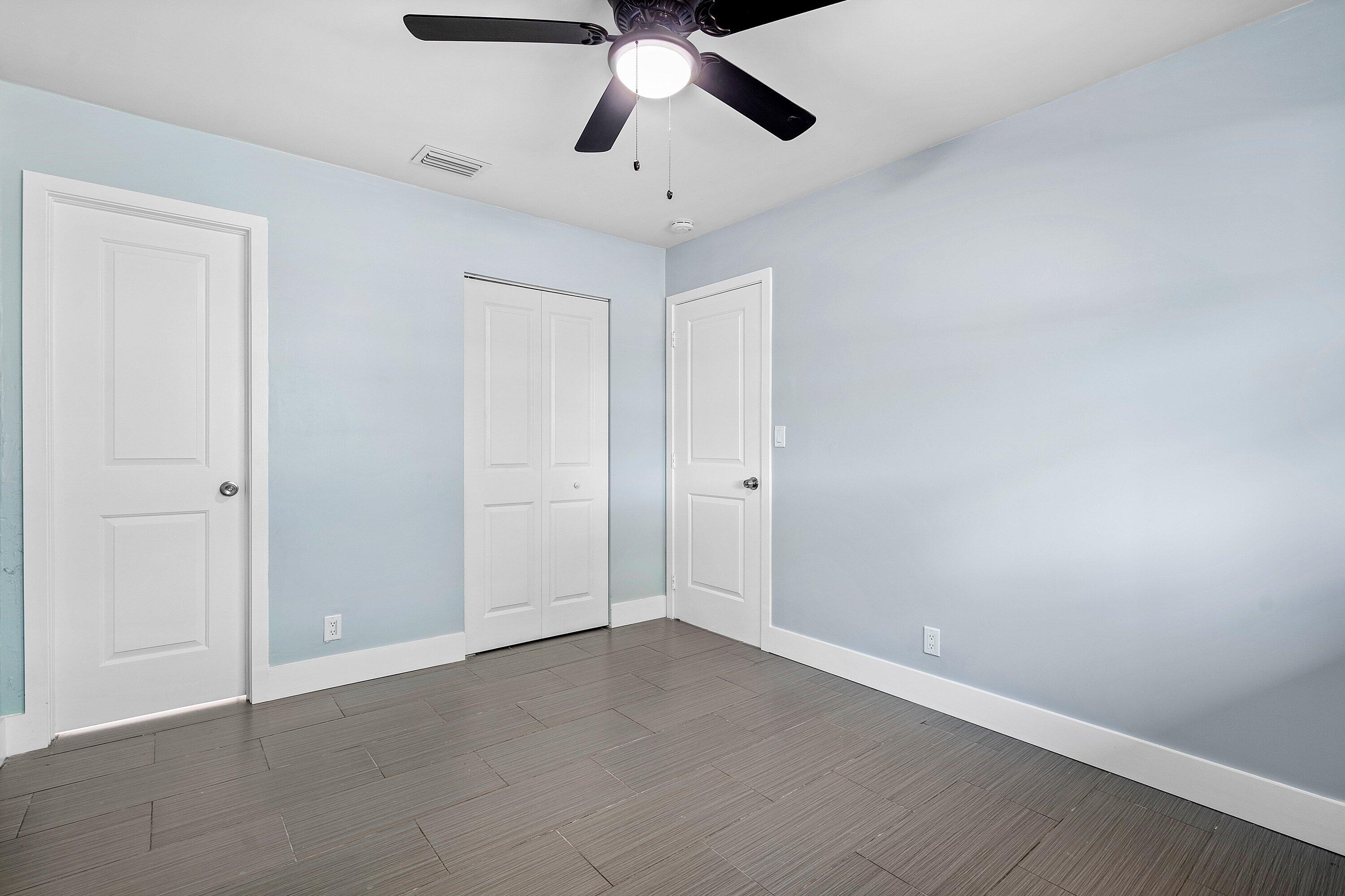 Interior space featuring wood-finish flooring, two-panel interior doors, a double-panel closet door, and a multi-blade ceiling fan with integrated lighting
