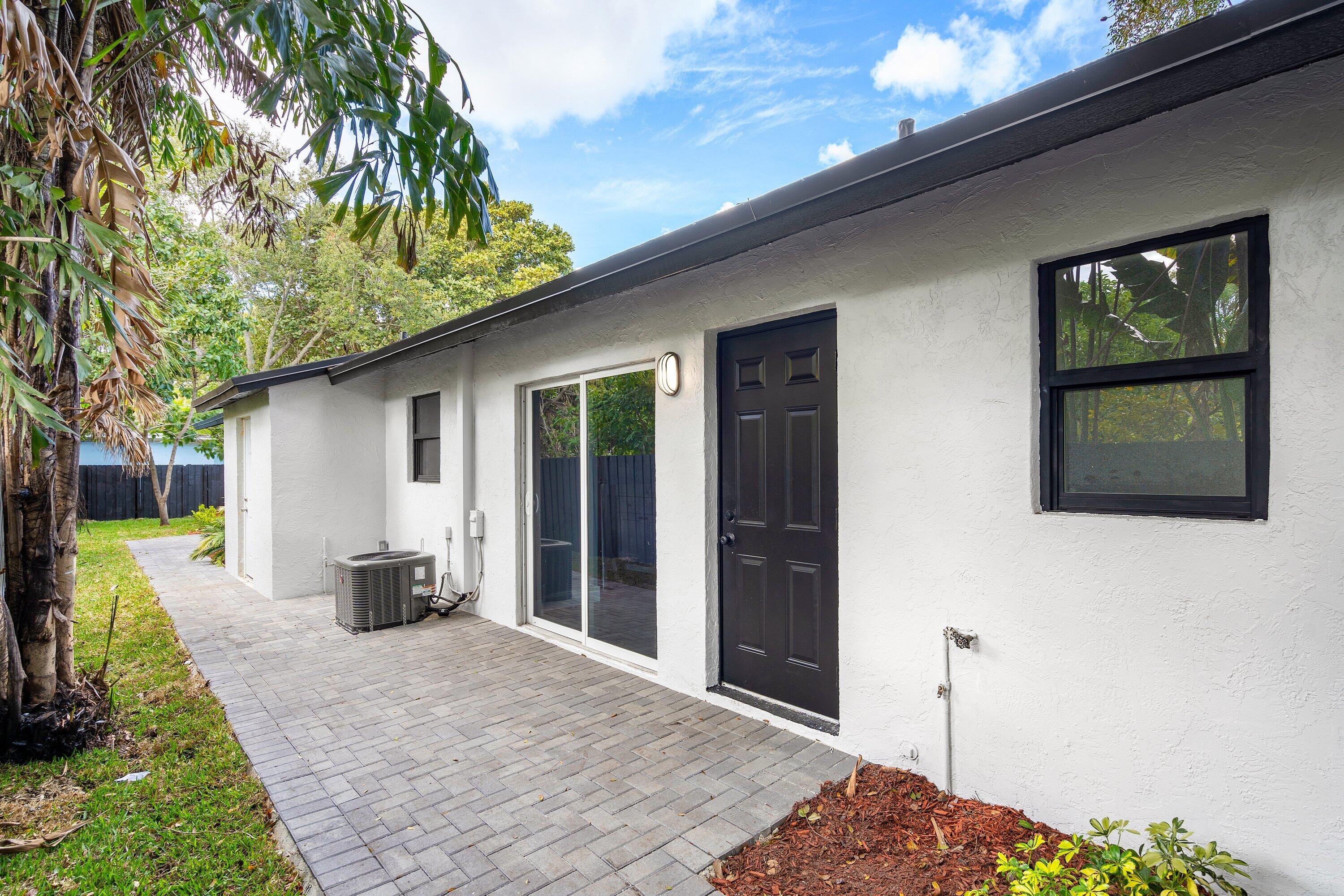Exterior featuring a paved brick patio, white stucco finish, sliding glass door, and dark-trimmed windows