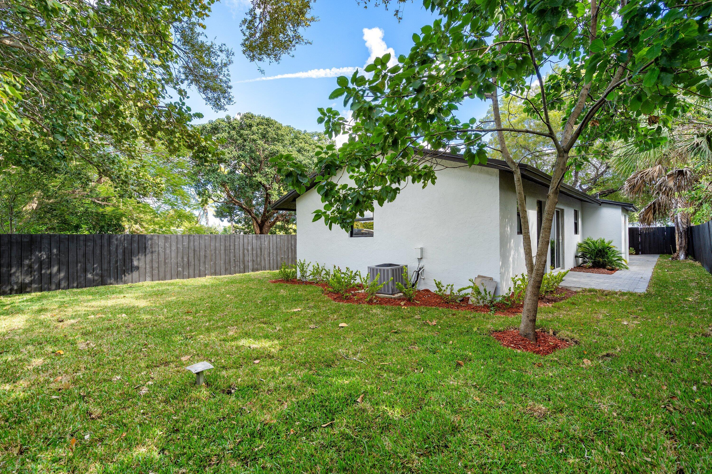Spacious backyard with manicured lawn, perimeter wood fencing, mature trees, landscaped mulch beds, and paved patio space