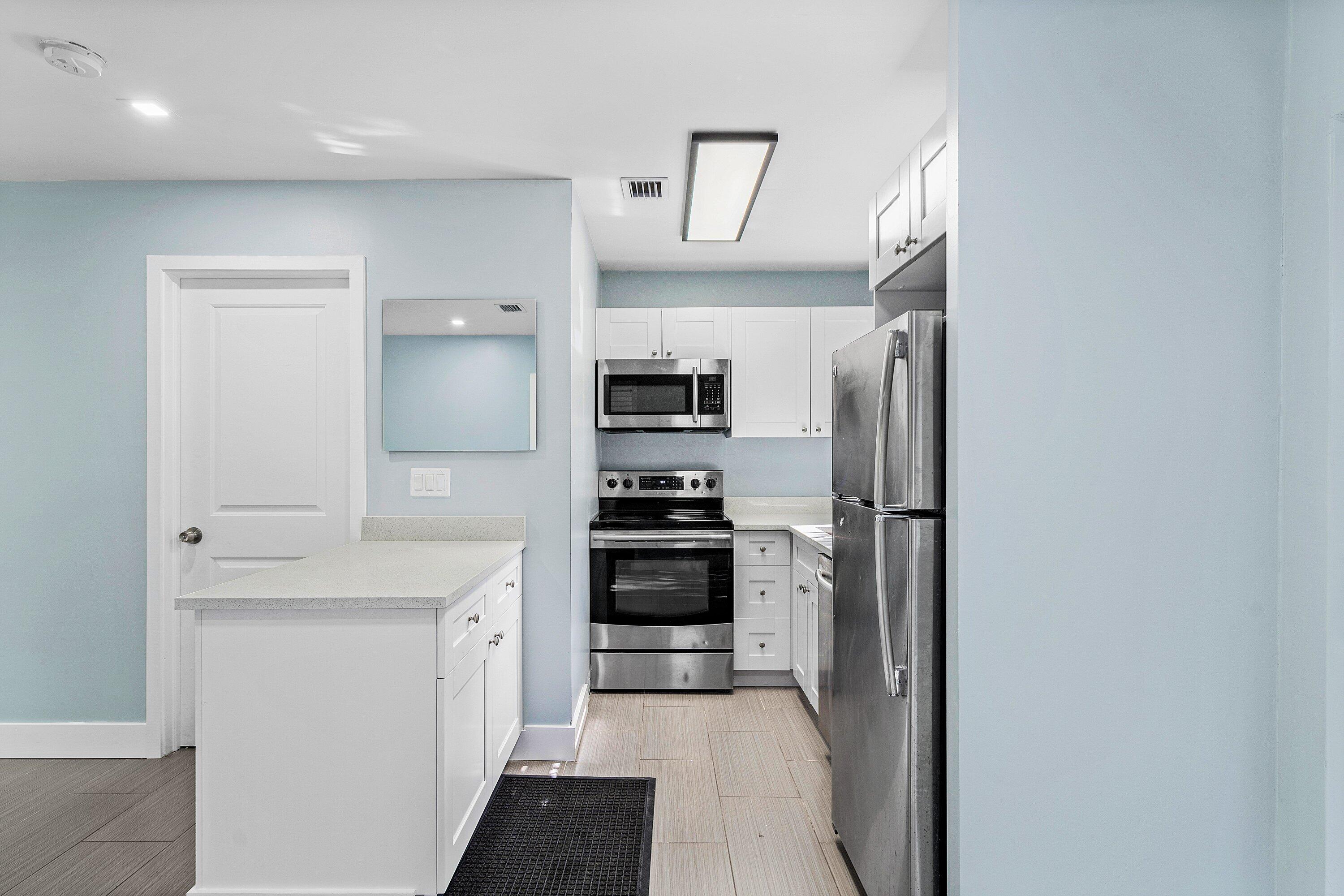 Kitchen featuring white cabinetry, solid-surface countertops, stainless steel appliances, and tile flooring