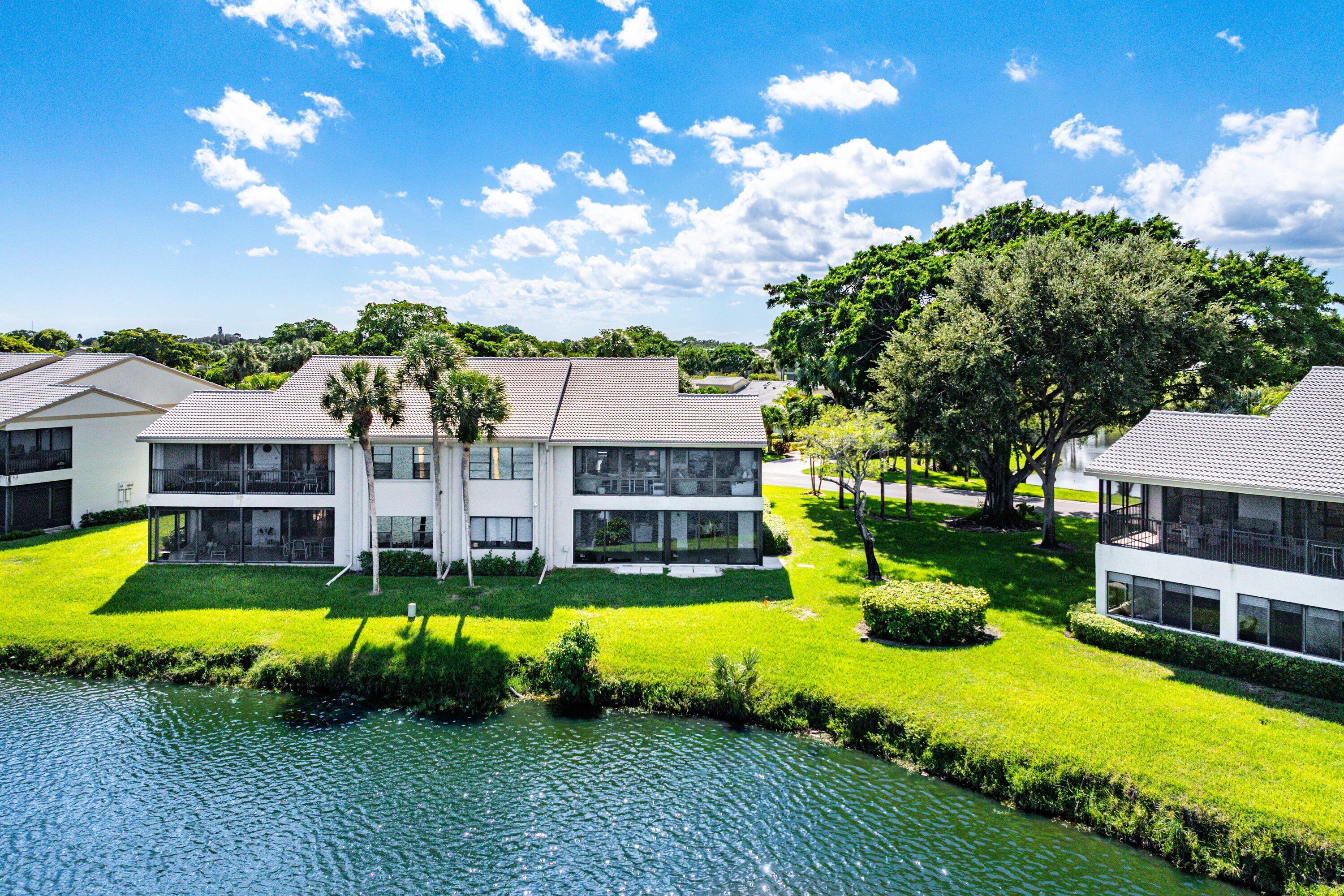 Multi-story building featuring screened-in lanais, tile roofing, manicured green space, and waterfront frontage