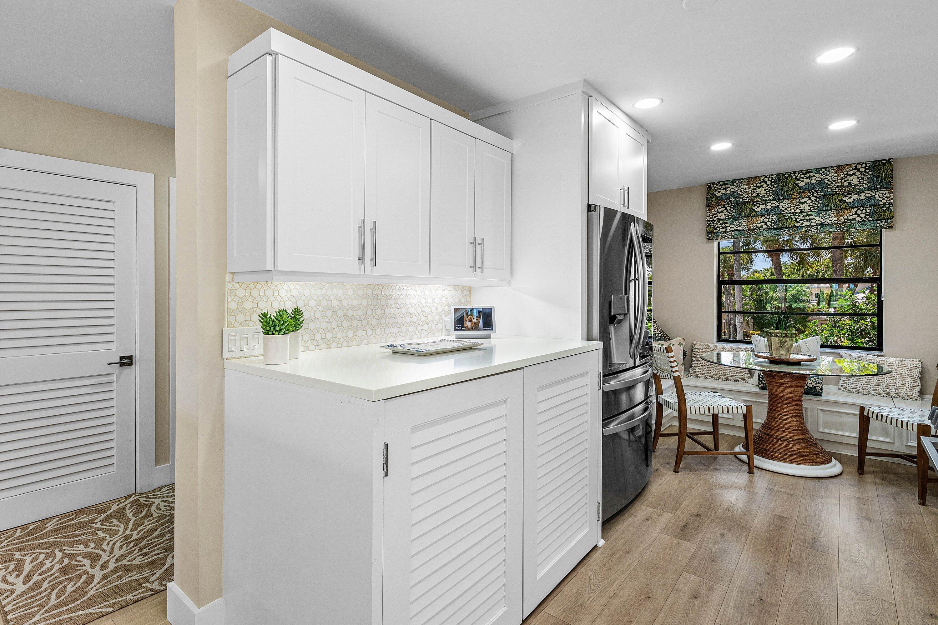 Kitchen cabinetry featuring white shaker-style doors, stone-finish countertops, geometric mosaic tile backsplash, stainless steel refrigerator, and wood-finish flooring