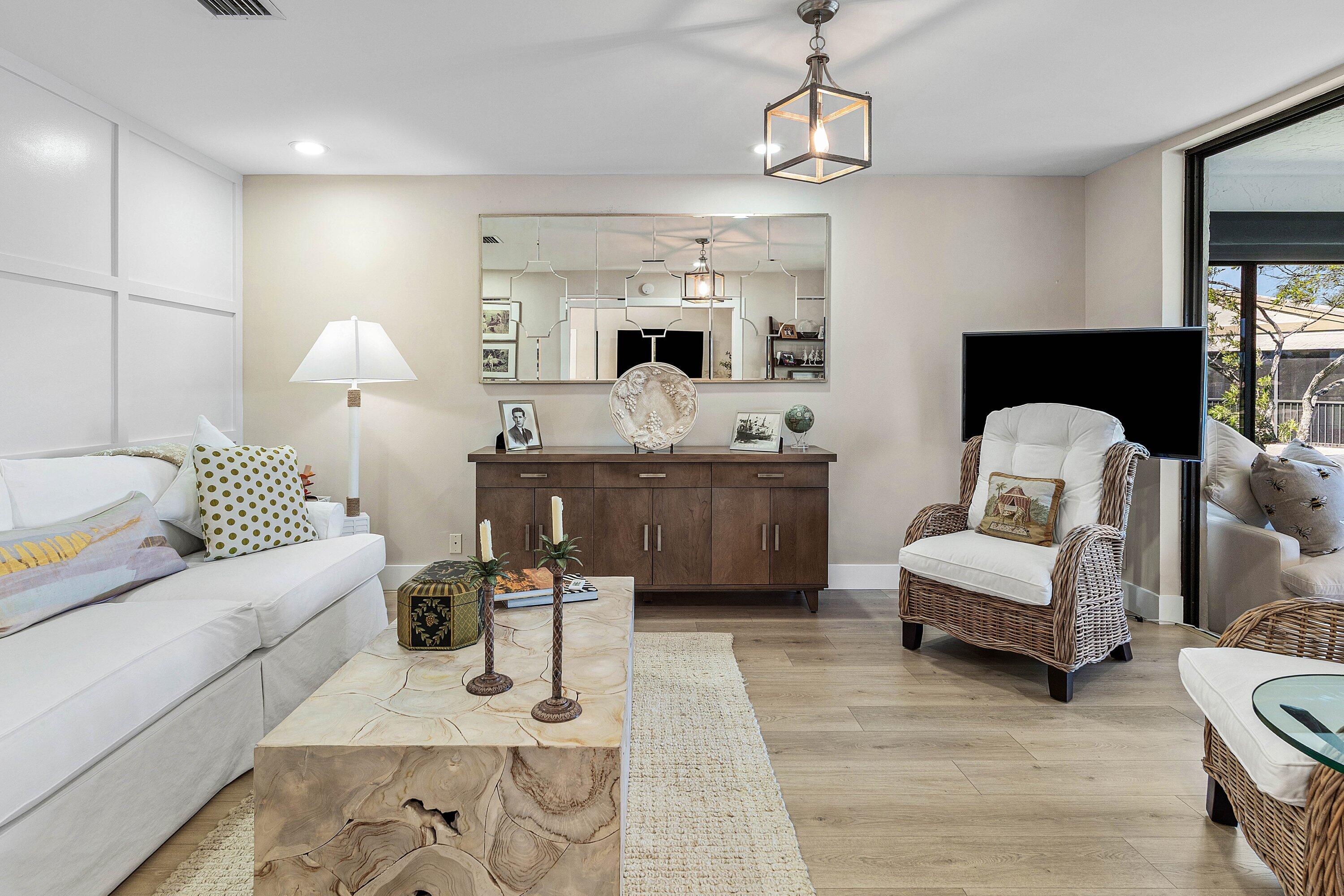 Living area featuring wood-finish flooring, grid-pattern wall molding, large decorative wall mirror, and modern geometric pendant lighting Living area featuring wood-finish flooring, grid-pattern wall molding, large decorative wall mirror, and modern geometric pendant lighting