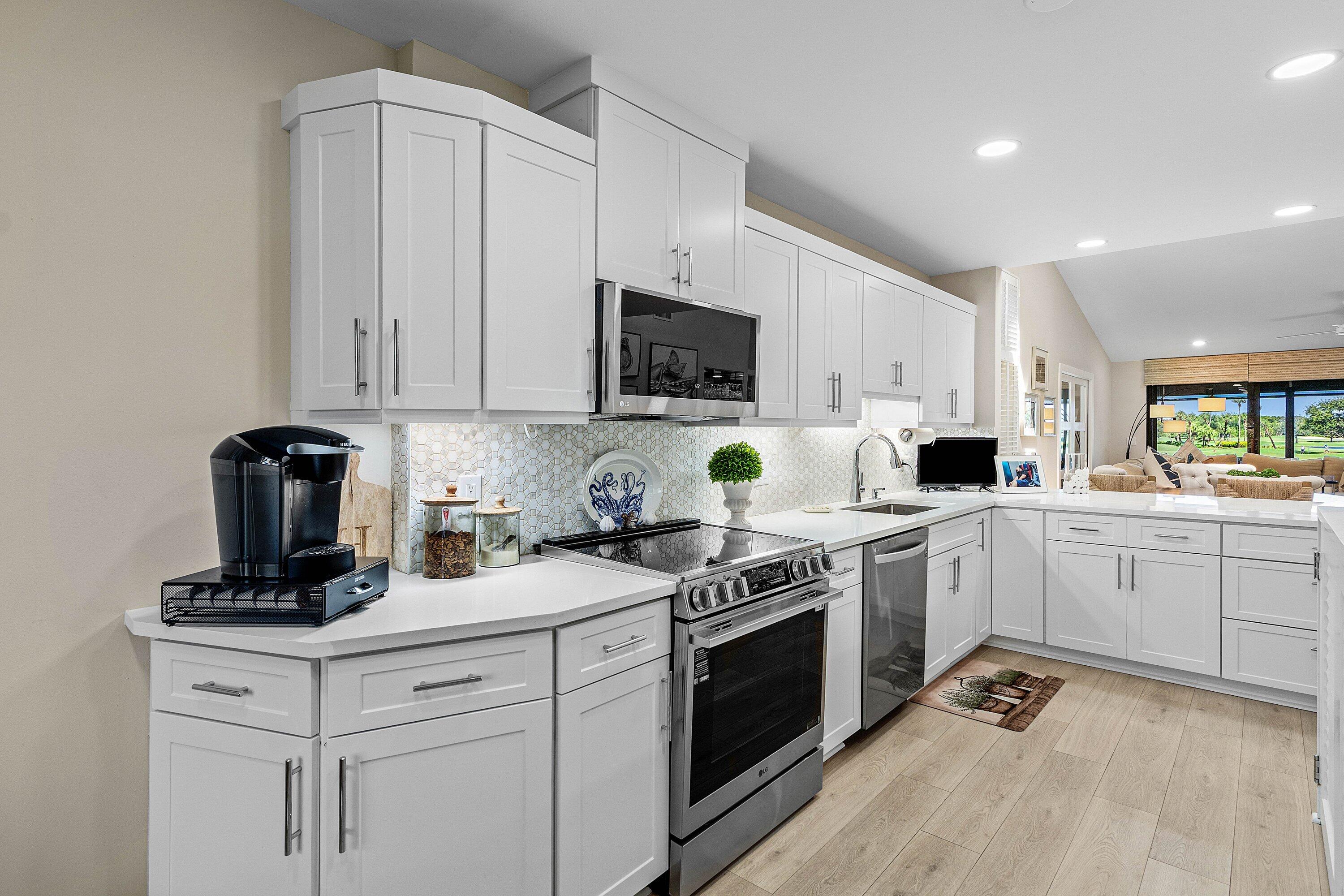 Kitchen featuring white Shaker-style cabinetry, quartz countertops, a patterned tile backsplash, stainless steel appliances, and wood-finish flooring