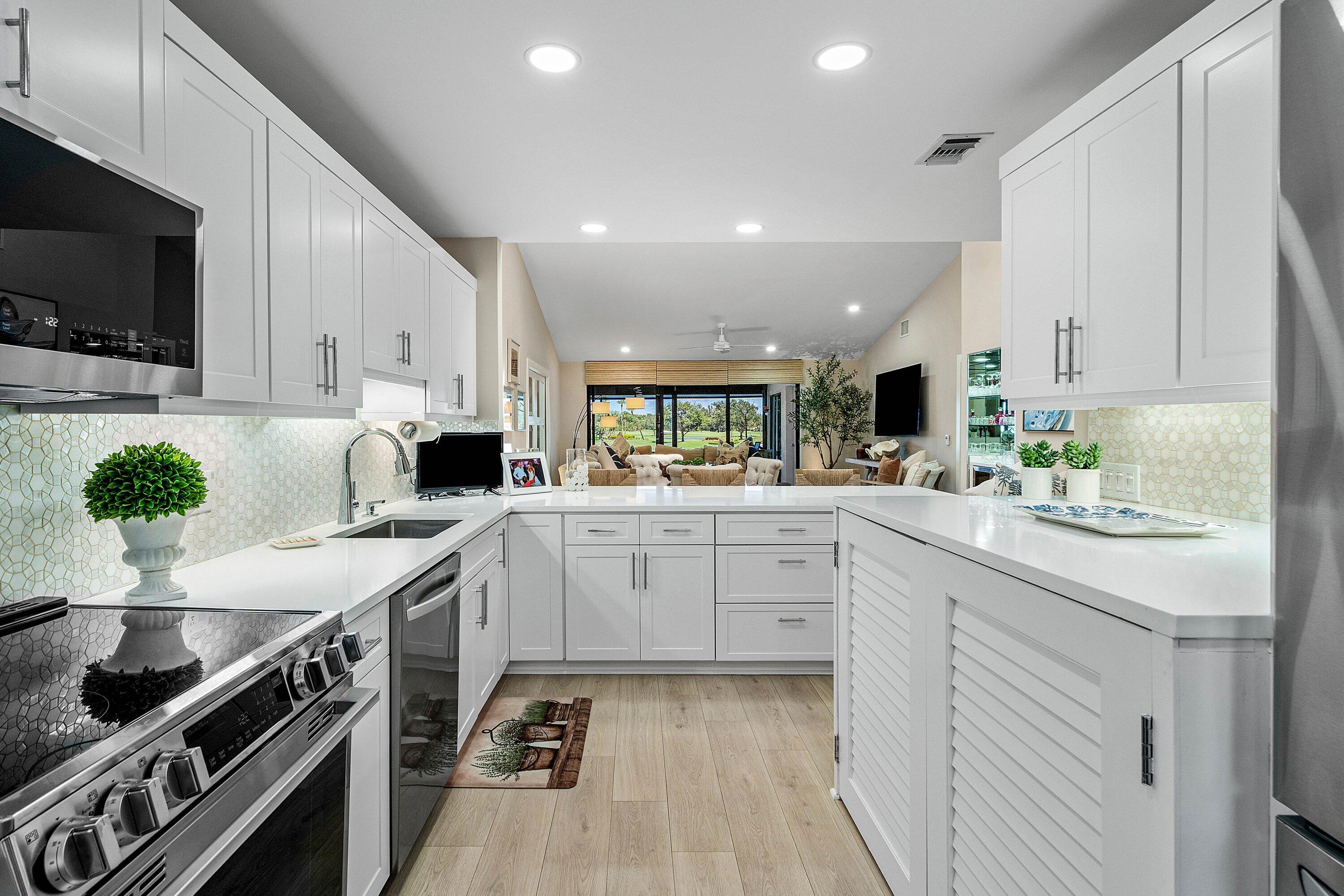Kitchen featuring white shaker-style cabinetry, solid-surface countertops, a geometric patterned backsplash, stainless steel appliances, and wood-finish flooring