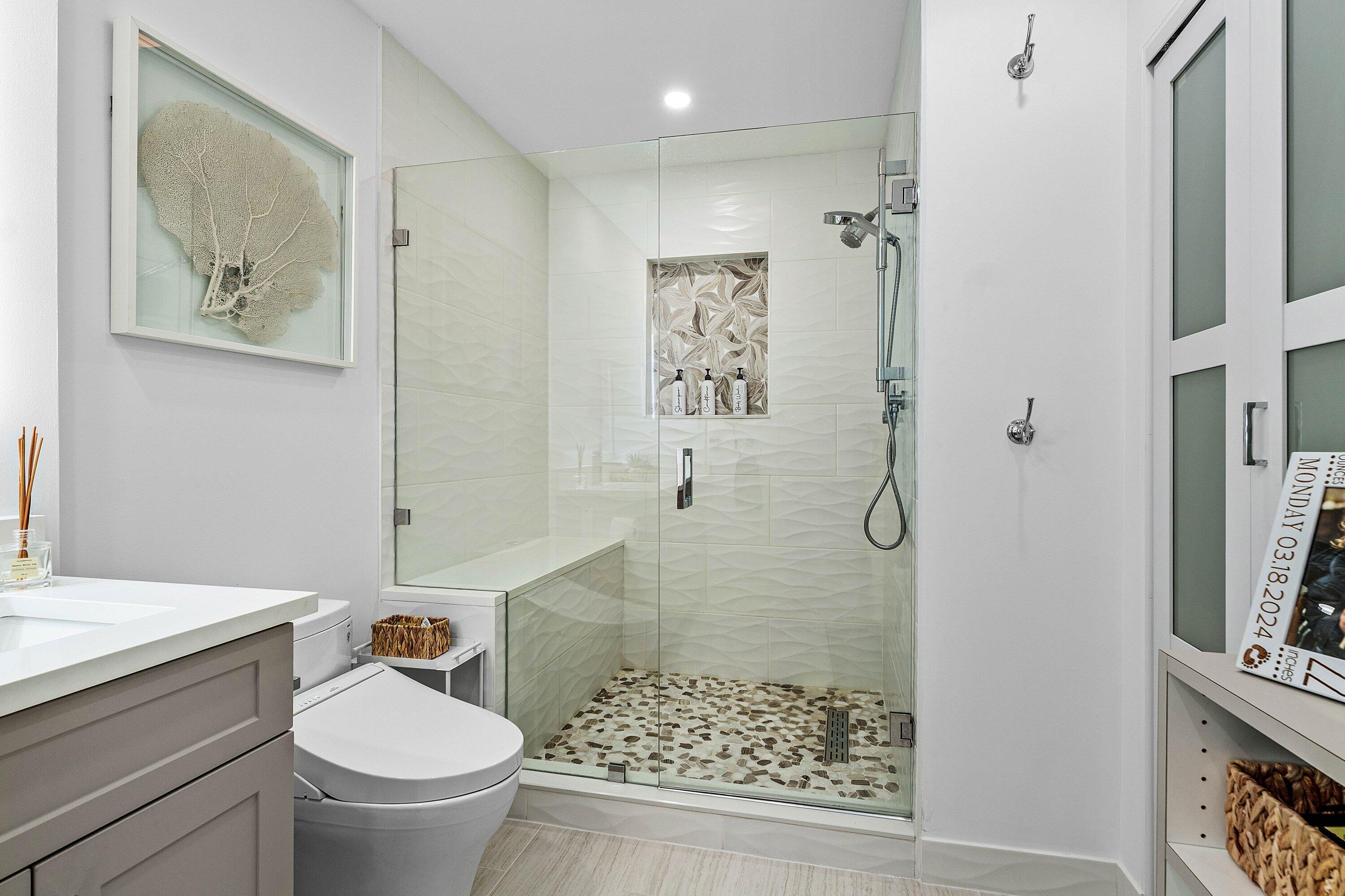 Walk-in shower featuring a frameless glass enclosure, pebble-stone flooring, built-in bench, and textured tile wall surround with a recessed niche