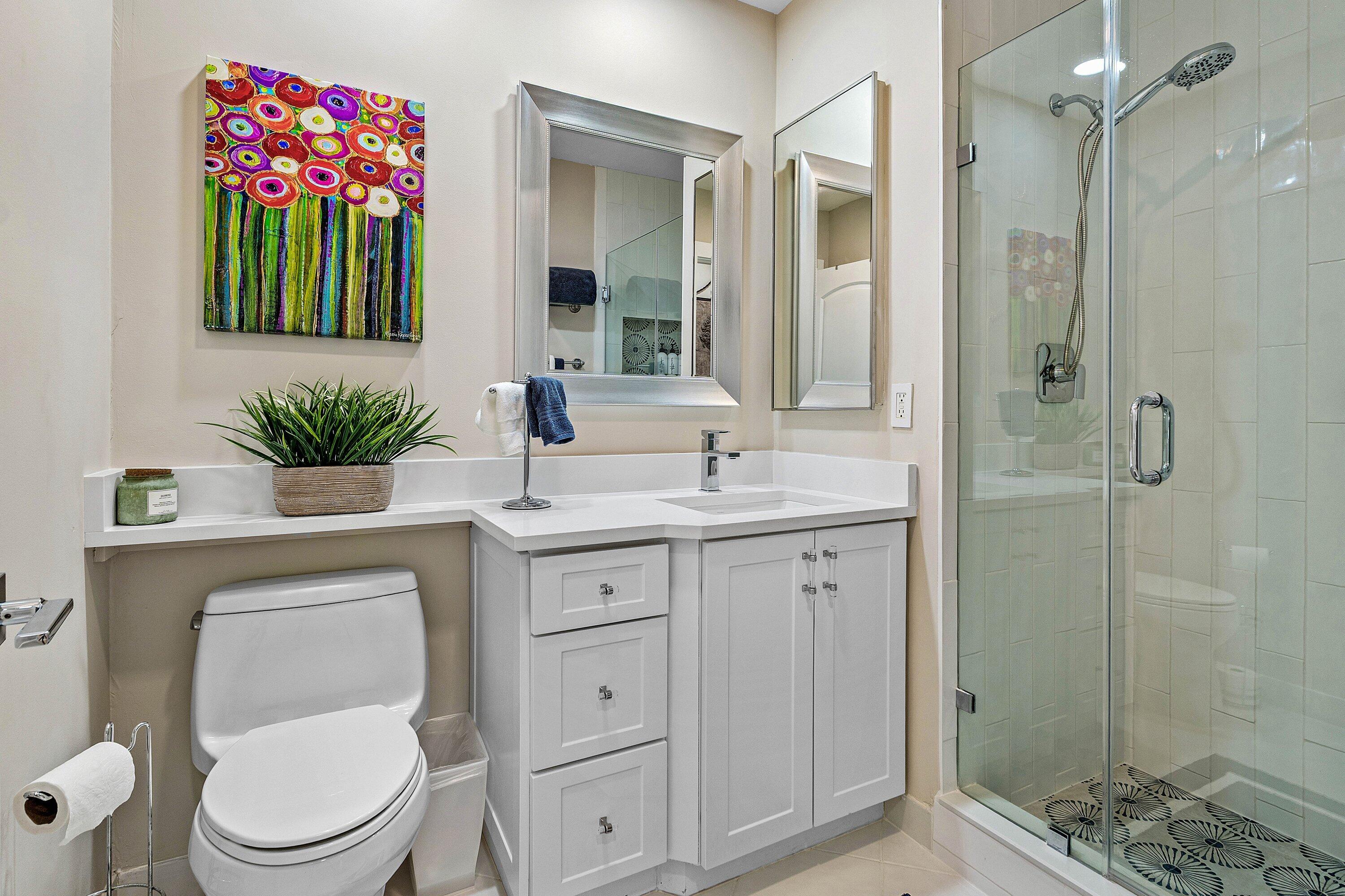 Bathroom featuring a white vanity cabinet with quartz countertops, an undermount sink, a glass-enclosed shower with tiled walls, and a wall-mounted medicine cabinet