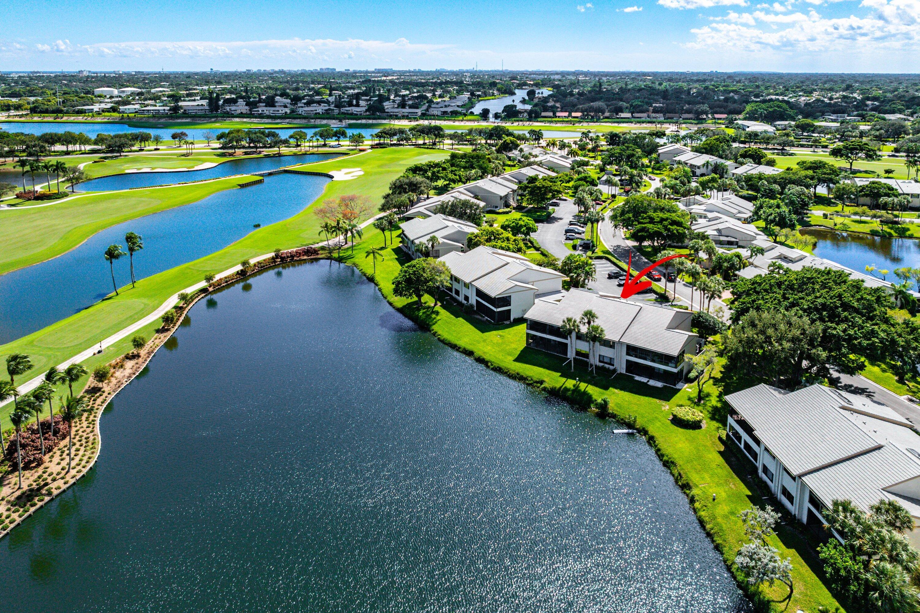 Aerial perspective of a multi-story building featuring a hipped roof, situated on a waterfront lot with grass lawns, mature landscaping, and proximity to a golf course Aerial perspective of a multi-story building featuring a hipped roof, situated on a waterfront lot with grass lawns, mature landscaping, and proximity to a golf course