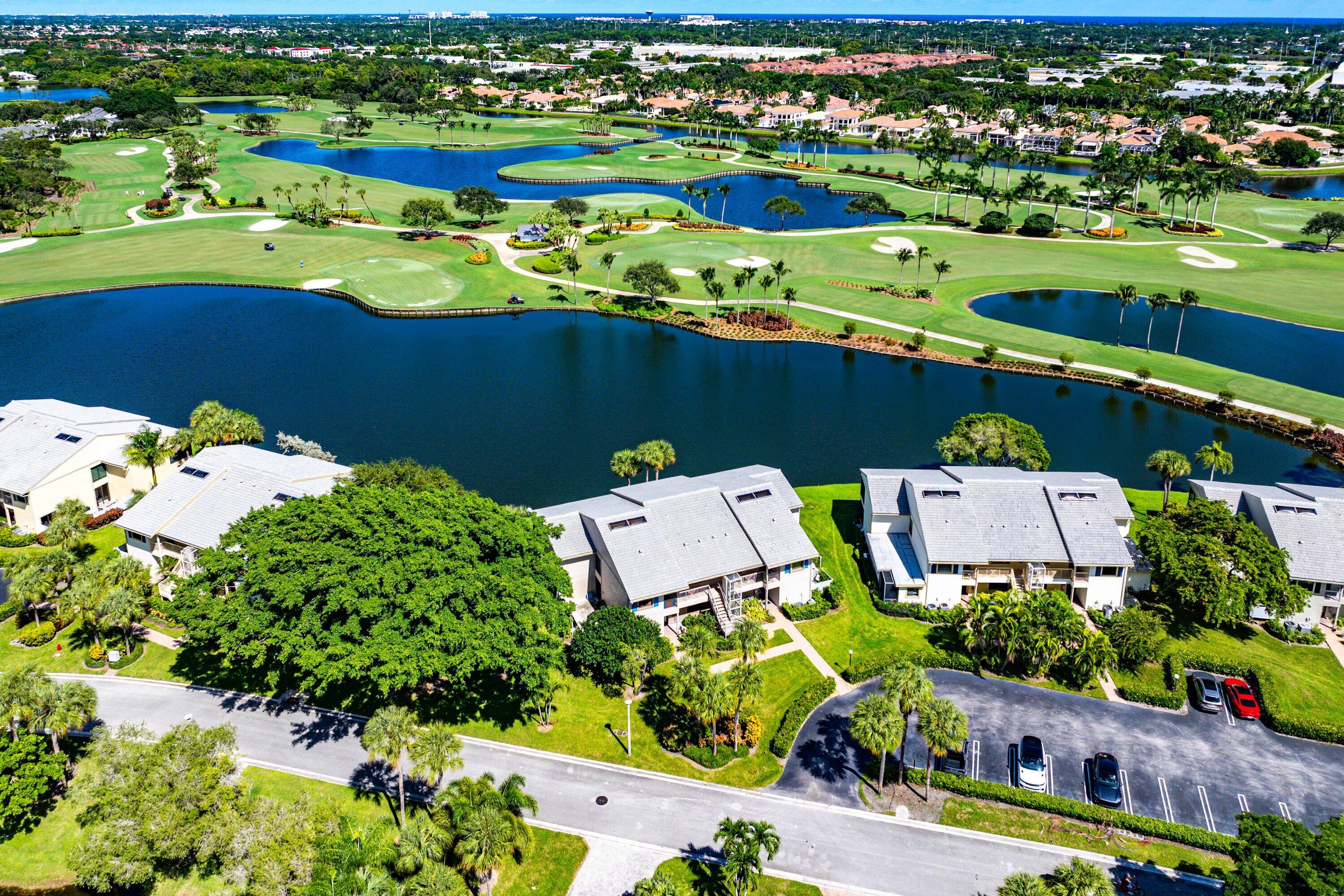 Aerial perspective featuring multi-story residential buildings with shingle-style roofing, situated along a expansive water feature, bordered by professional landscaping and mature trees
