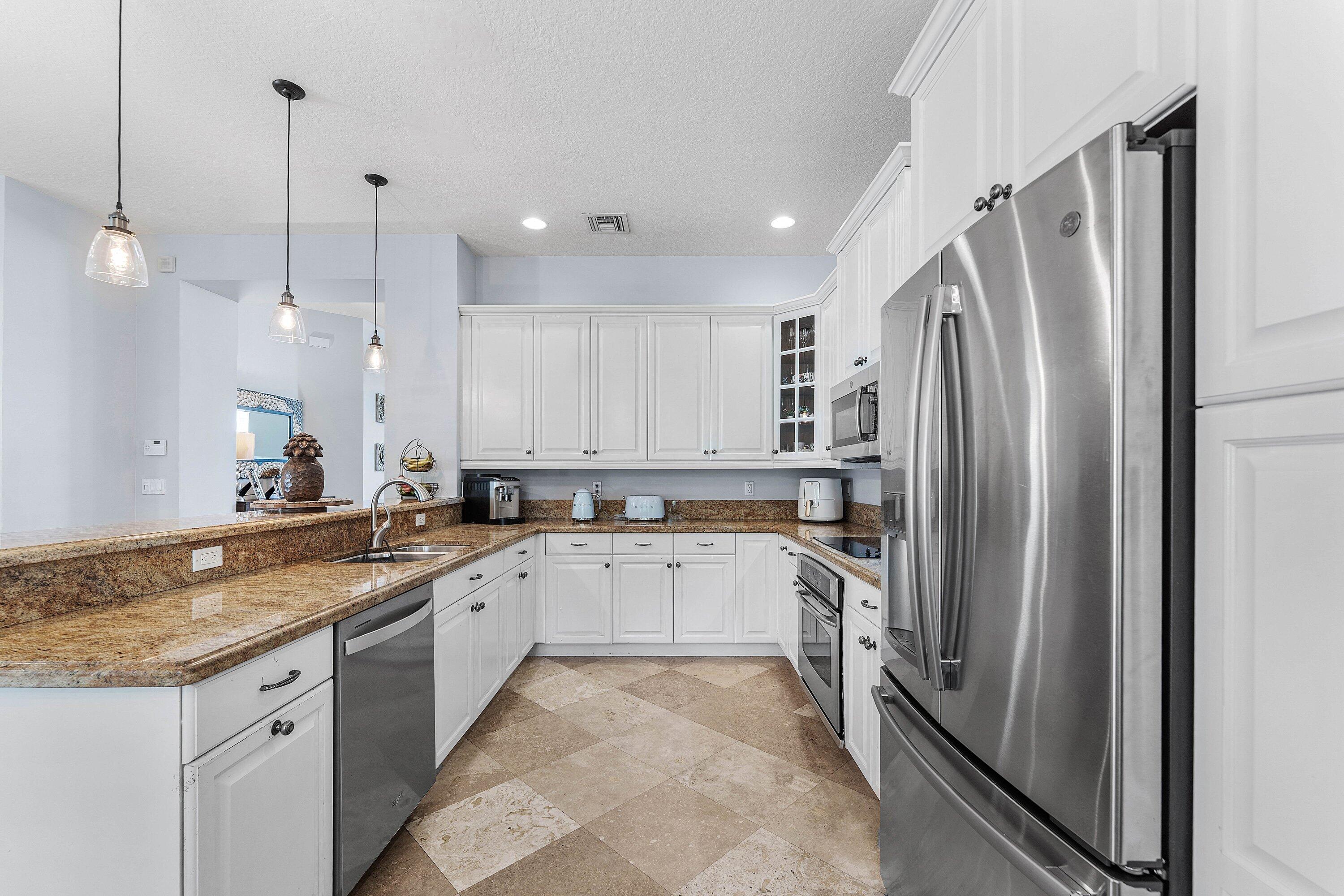 Spacious gourmet kitchen featuring white cabinetry, stainless steel appliances, granite countertops, a large center island, and abundant natural light.