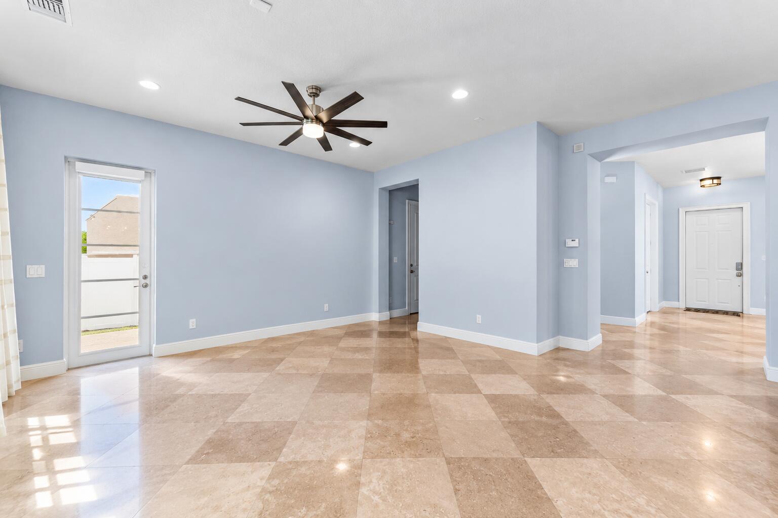 Open-concept family room with high ceilings, sleek modern ceiling fan, polished tile flooring, and plenty of natural light creating an inviting living space.