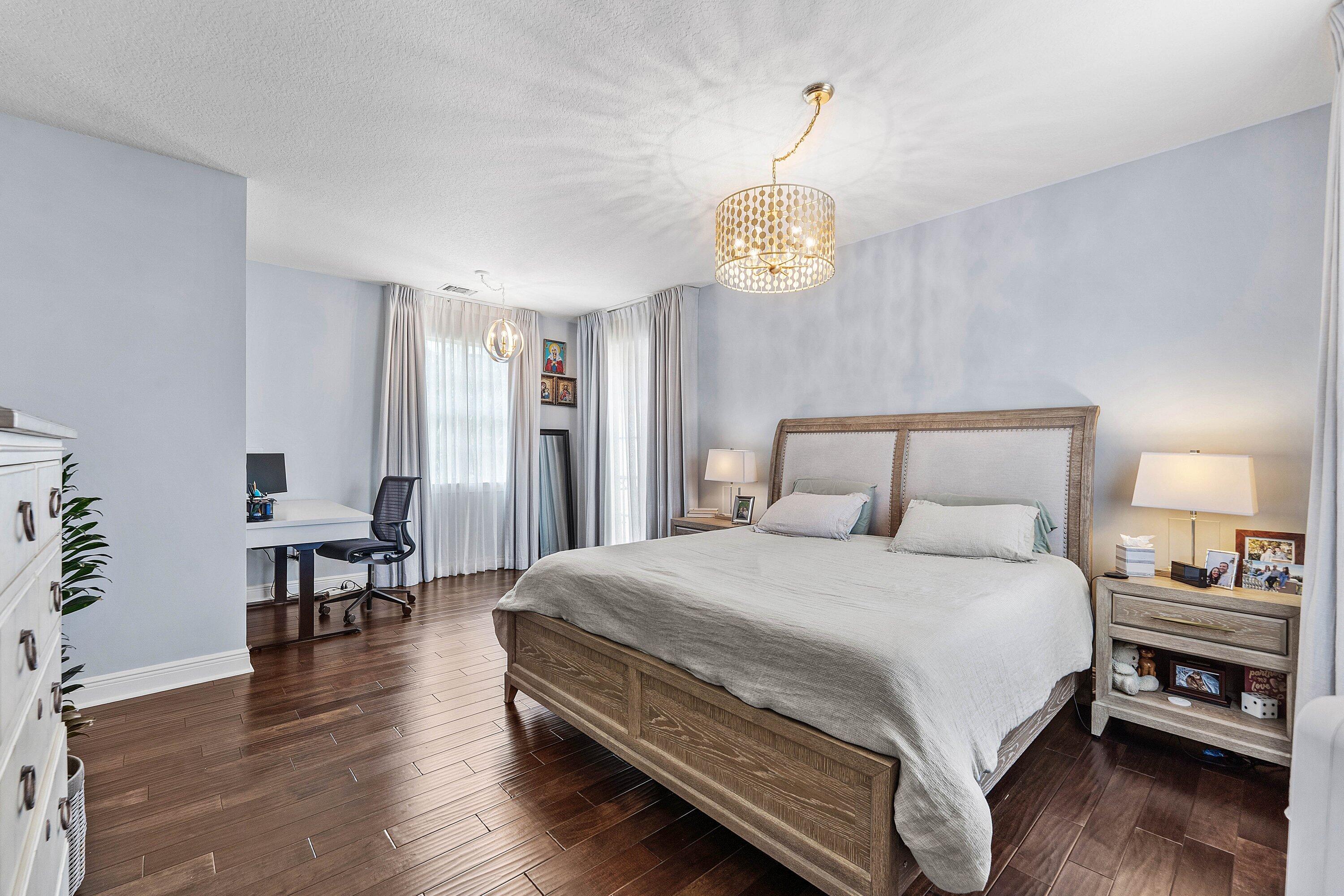 Spacious master bedroom with rich wood flooring, elegant lighting, abundant natural light, and a stylish sitting area.