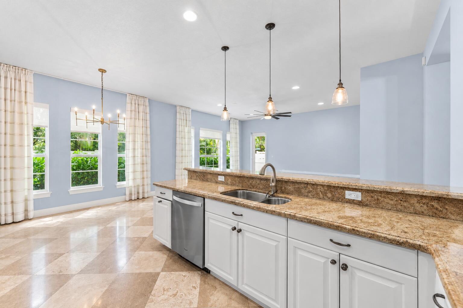 Bright open-concept kitchen with oversized island, granite countertops, white cabinetry, stainless steel appliances, and seamless flow into the living area.