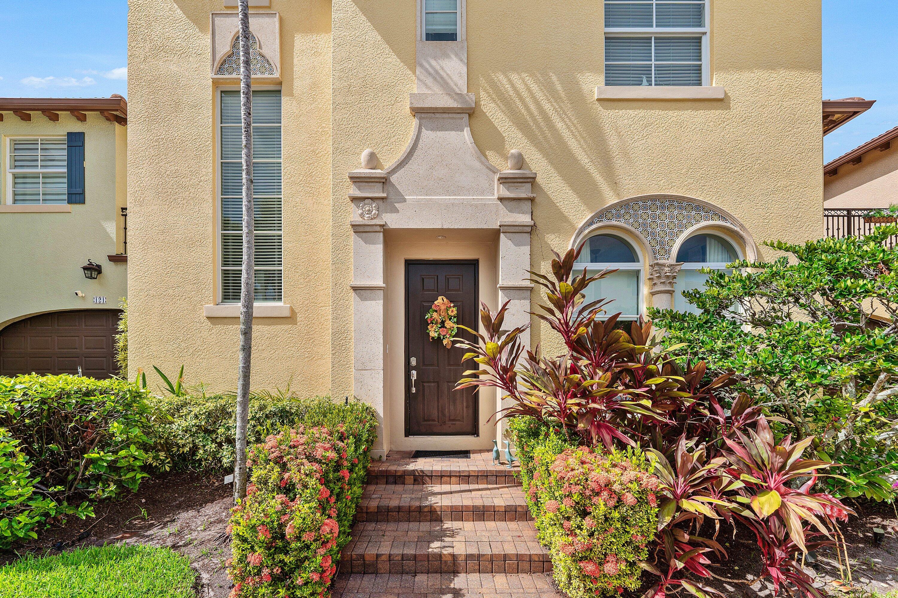 Welcoming front entry featuring an elegant arched doorway, decorative architectural details, and tropical landscaping.