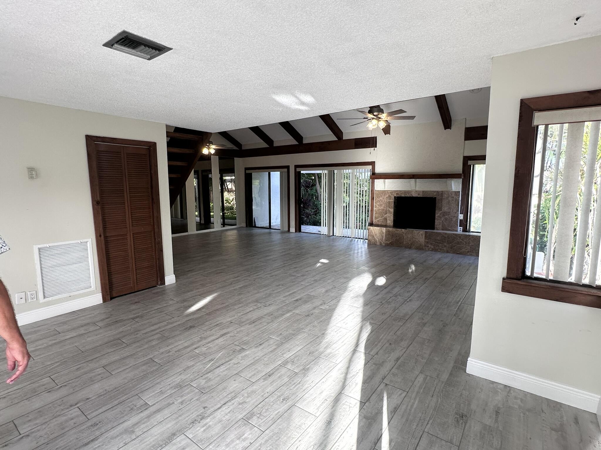 Open-concept interior featuring wood-finish flooring, exposed ceiling beams, a stone-surround fireplace, and multiple sliding glass doors