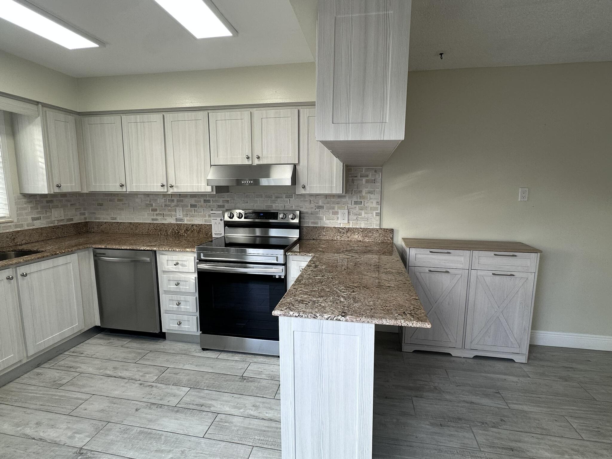 Kitchen featuring light-finish cabinetry, stone-texture countertops, stainless steel appliances, a subway-style tiled backsplash, and wood-finish tile flooring