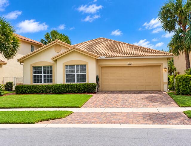 Charming single-story home featuring a Spanish tile roof, brick paver driveway, attached 2-car garage, and manicured tropical landscaping.
