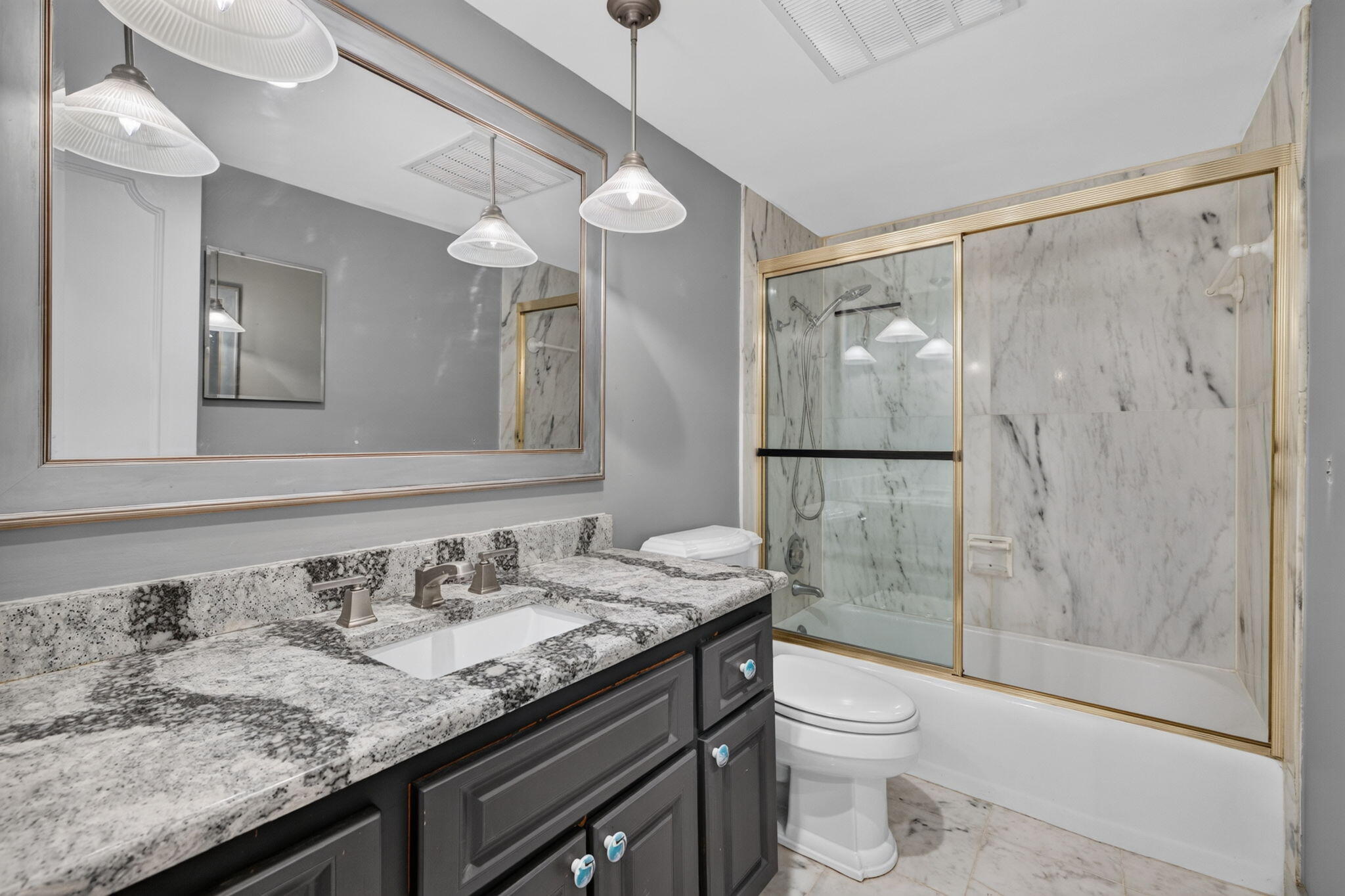 Granite countertop with integrated sink, dark wood-finish vanity, large framed mirror, glass-enclosed shower with tiled walls, and recessed ceiling lighting
