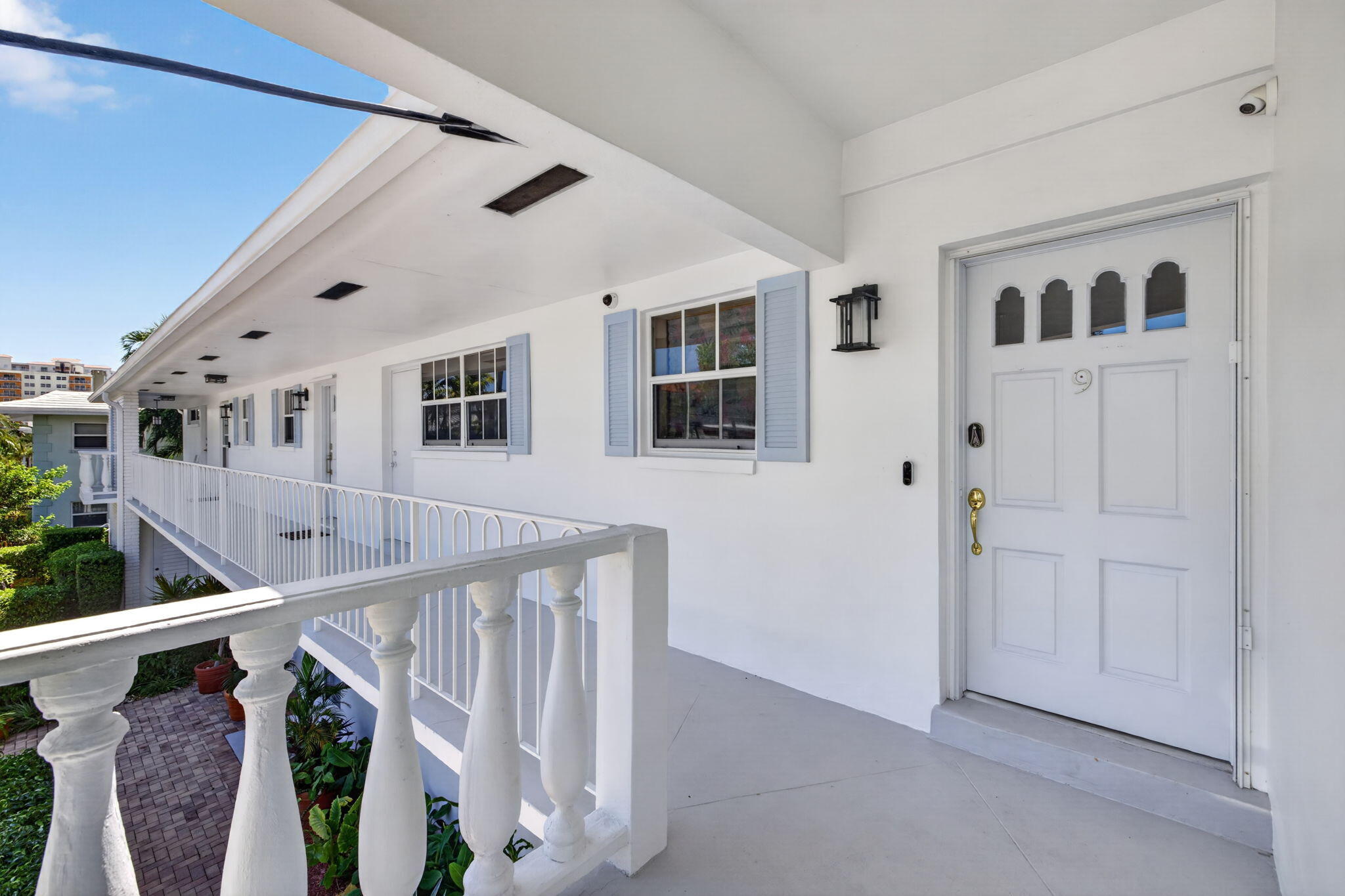 Exterior corridor access with white balustrade railing, light blue window shutters, and a paneled entry door with decorative glass inserts