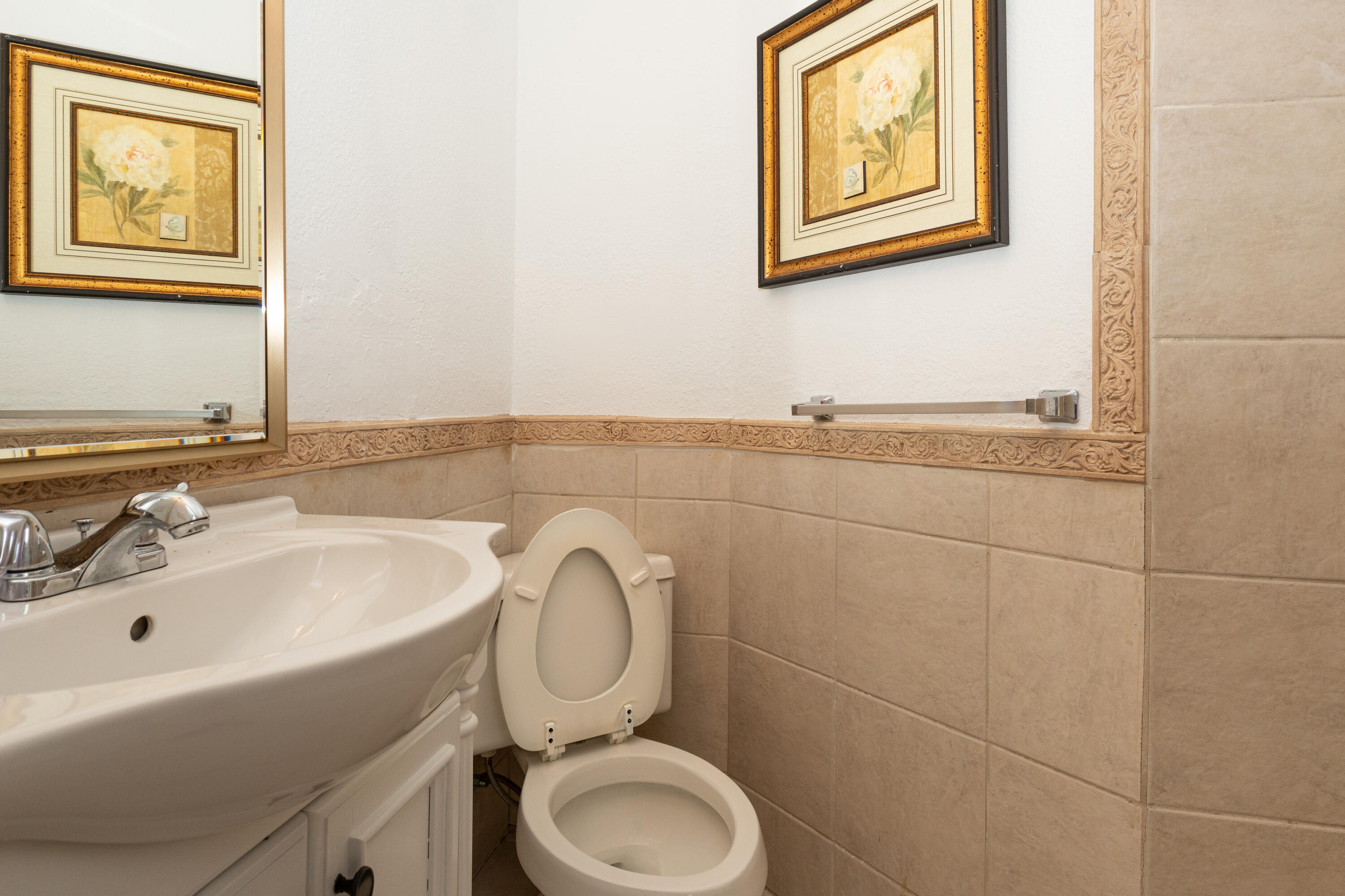 Powder room featuring a curved pedestal sink with chrome faucet, ceramic toilet, and tile walls accented with a decorative border
