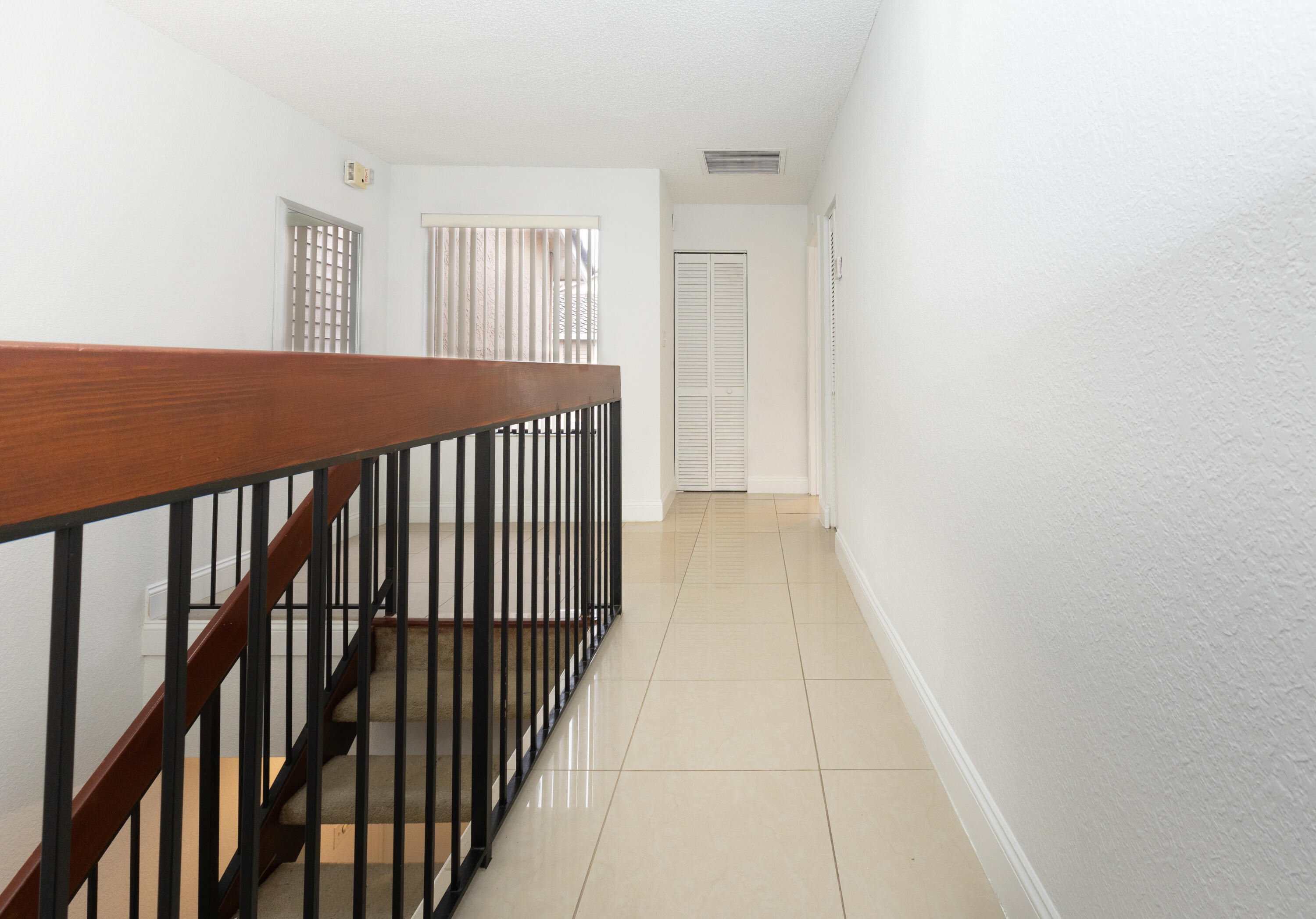 Wooden handrail with black metal balusters, tiled flooring, and a window with vertical blinds