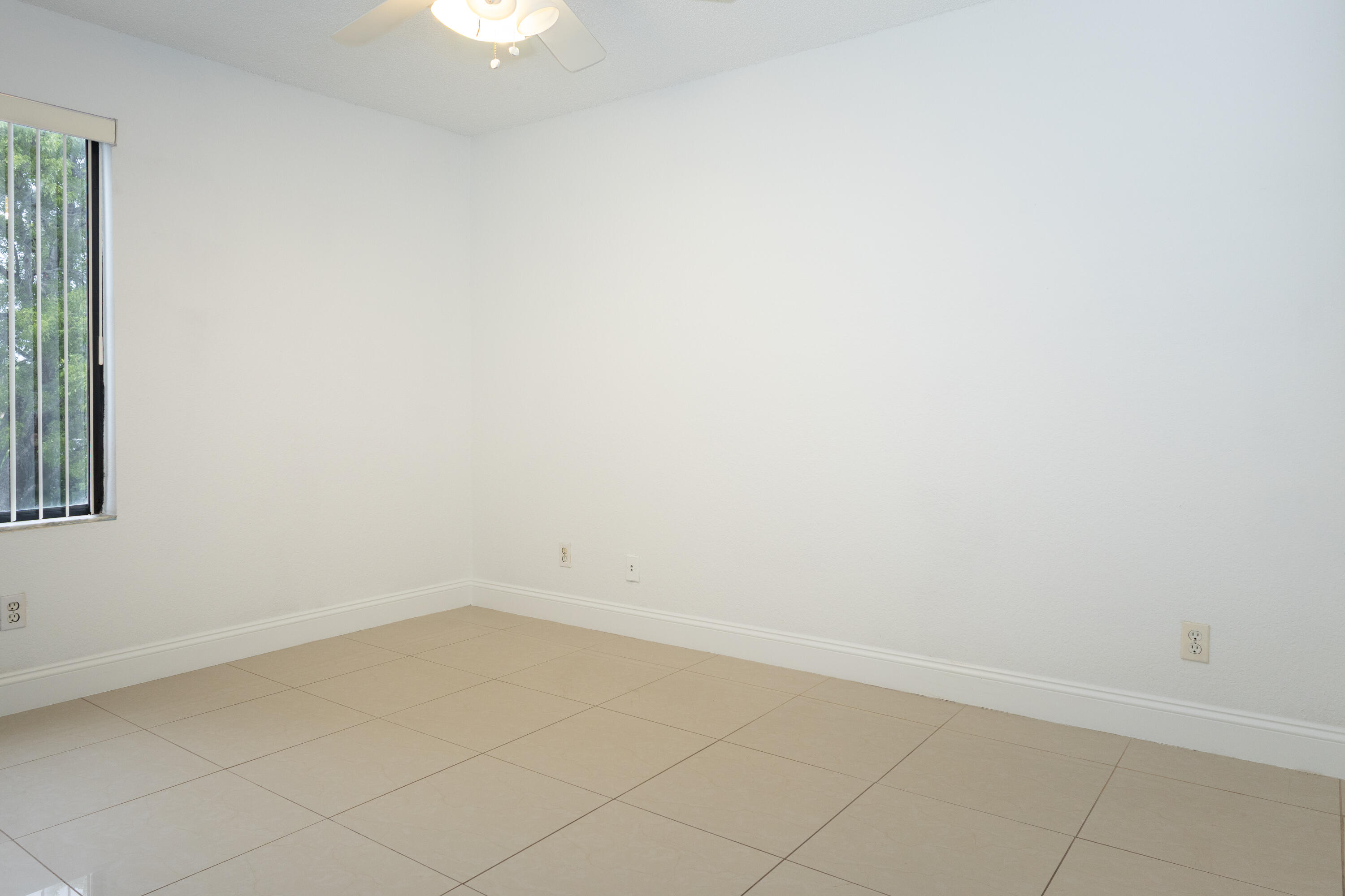 Bright, open room featuring neutral ceramic tile flooring throughout, recessed ceiling lighting, and abundant natural light from a window with security bars