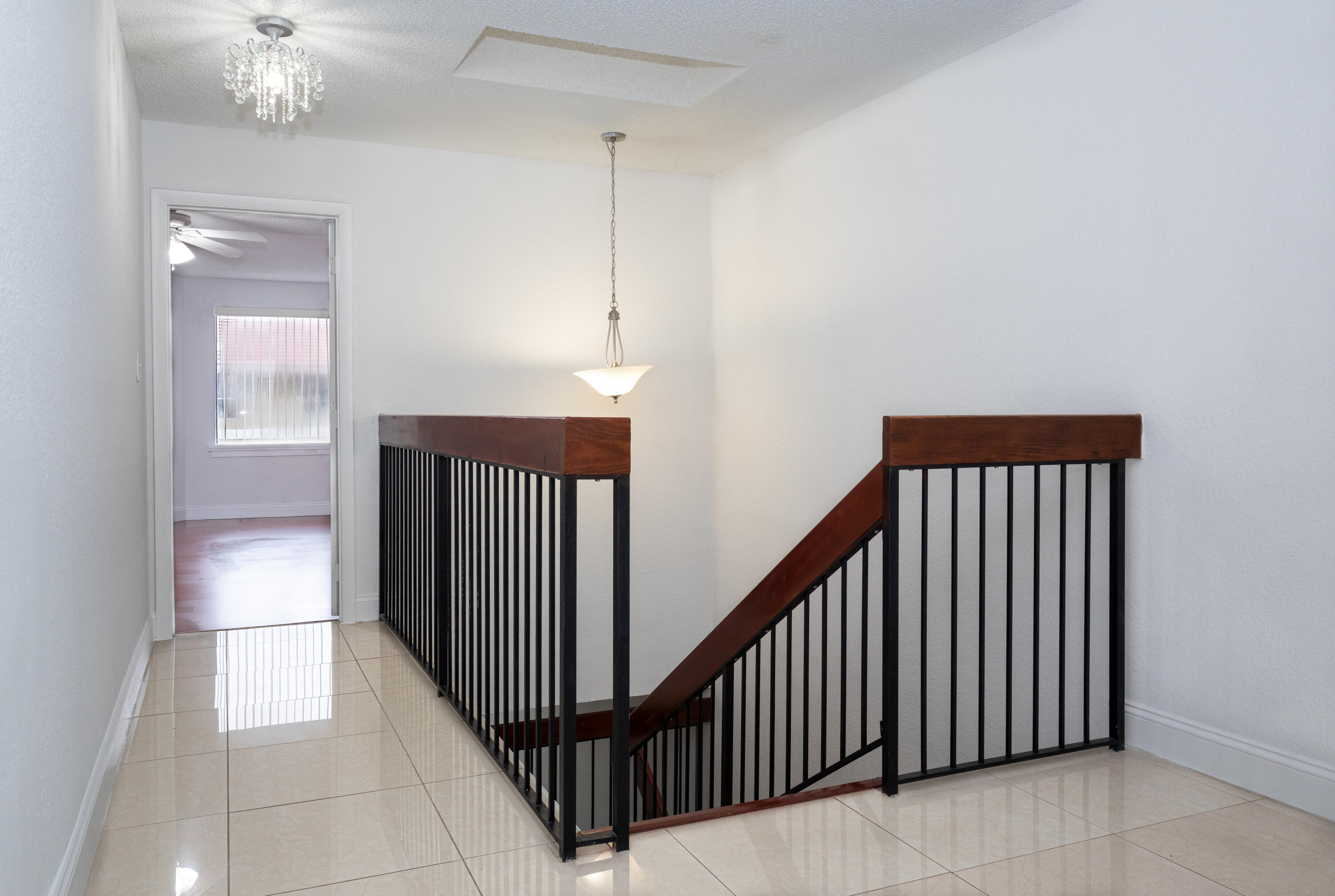Elegant staircase with dark wood railings and spindle detailing, polished tile flooring, and pendant lighting