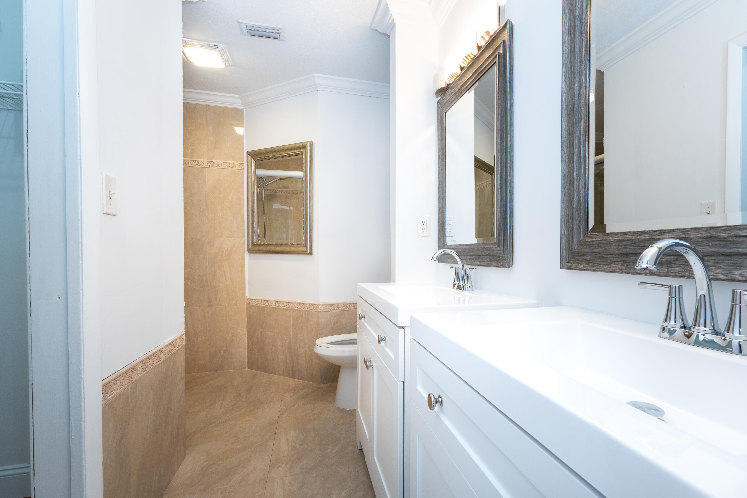 Dual vanities with integrated sinks, chrome fixtures, framed mirrors, crown molding, and tiled flooring