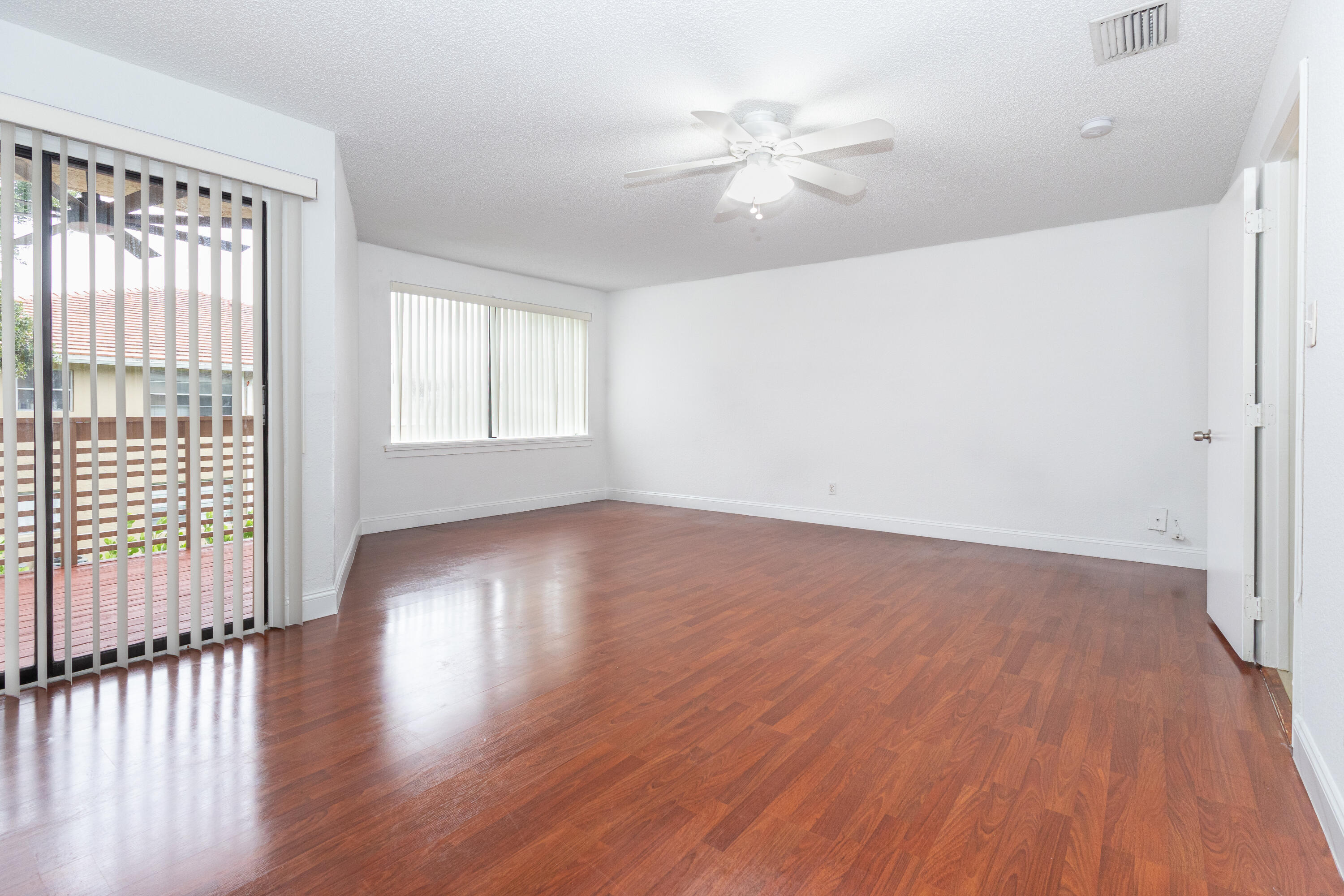 Spacious room with rich wood-finish flooring, abundant natural light from multiple windows, and a ceiling fan with recessed lighting