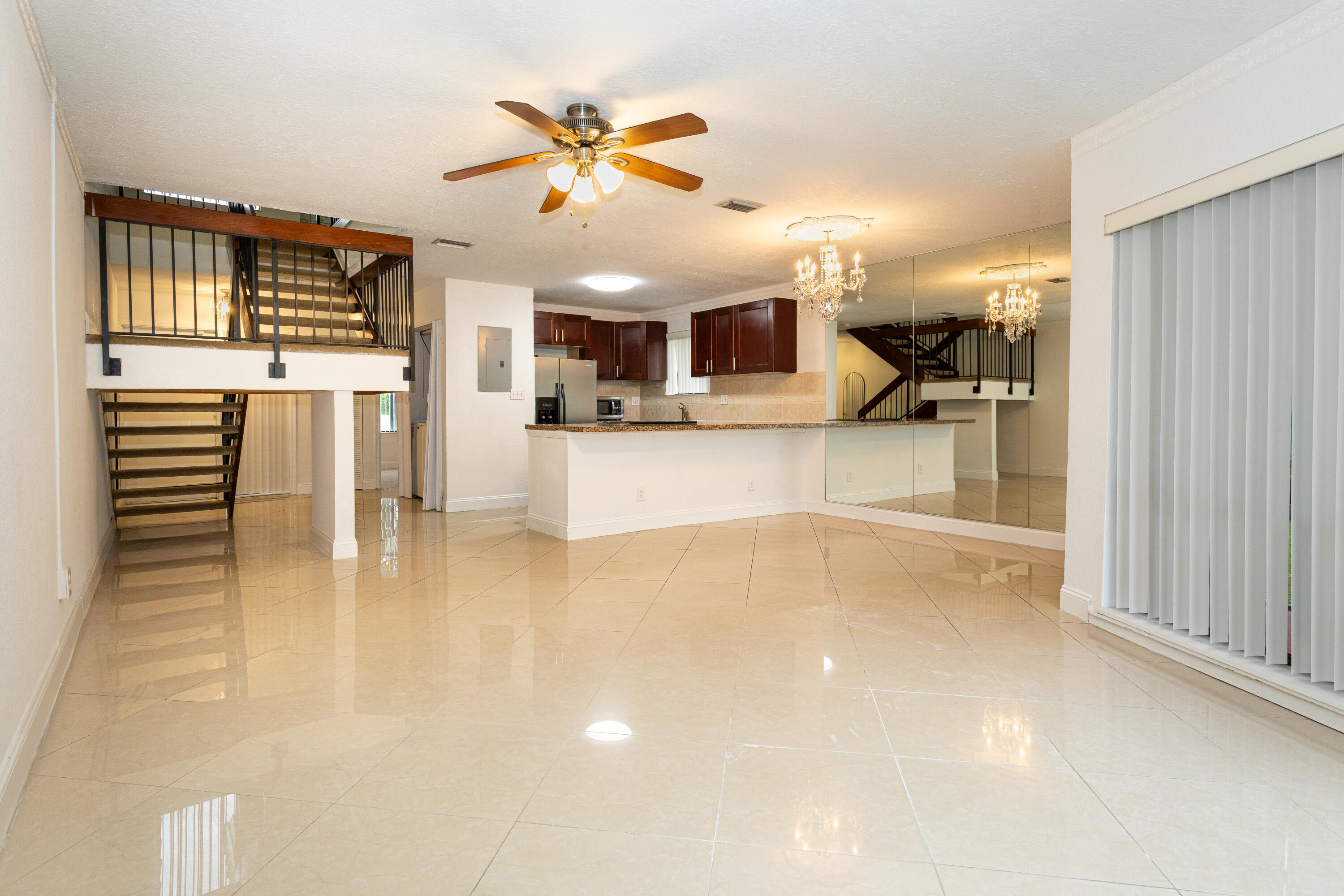 Expansive open-concept living area featuring large format tile flooring, a functional kitchen island, dark wood-finish cabinetry, and a ceiling fan Expansive open-concept living area featuring large format tile flooring, a functional kitchen island, dark wood-finish cabinetry, and a ceiling fan