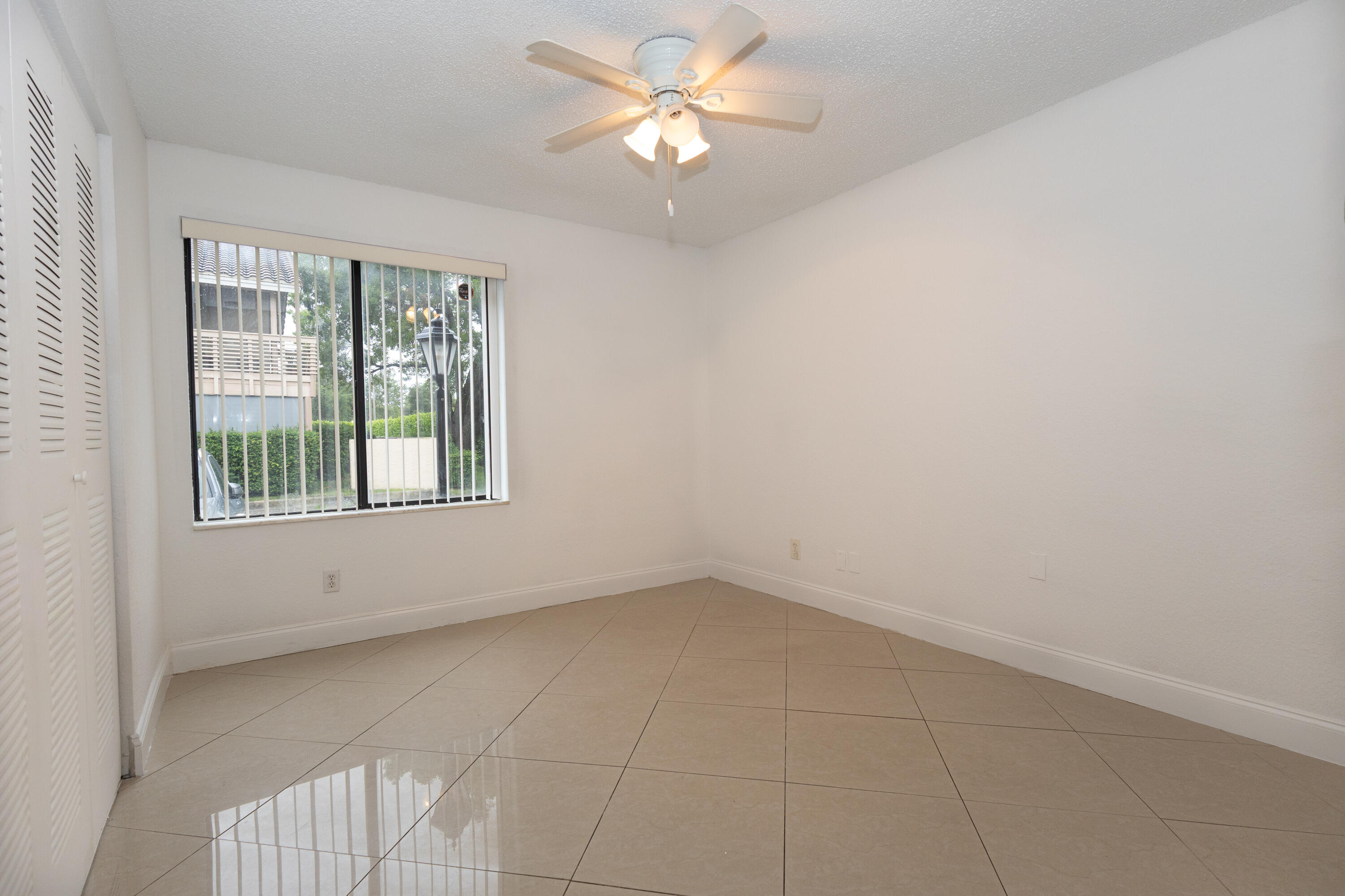 Bright, spacious bedroom featuring tile flooring throughout, a ceiling fan with integrated lighting, and large windows with security bars providing natural illumination and ventilation Bright, spacious bedroom featuring tile flooring throughout, a ceiling fan with integrated lighting, and large windows with security bars providing natural illumination and ventilation