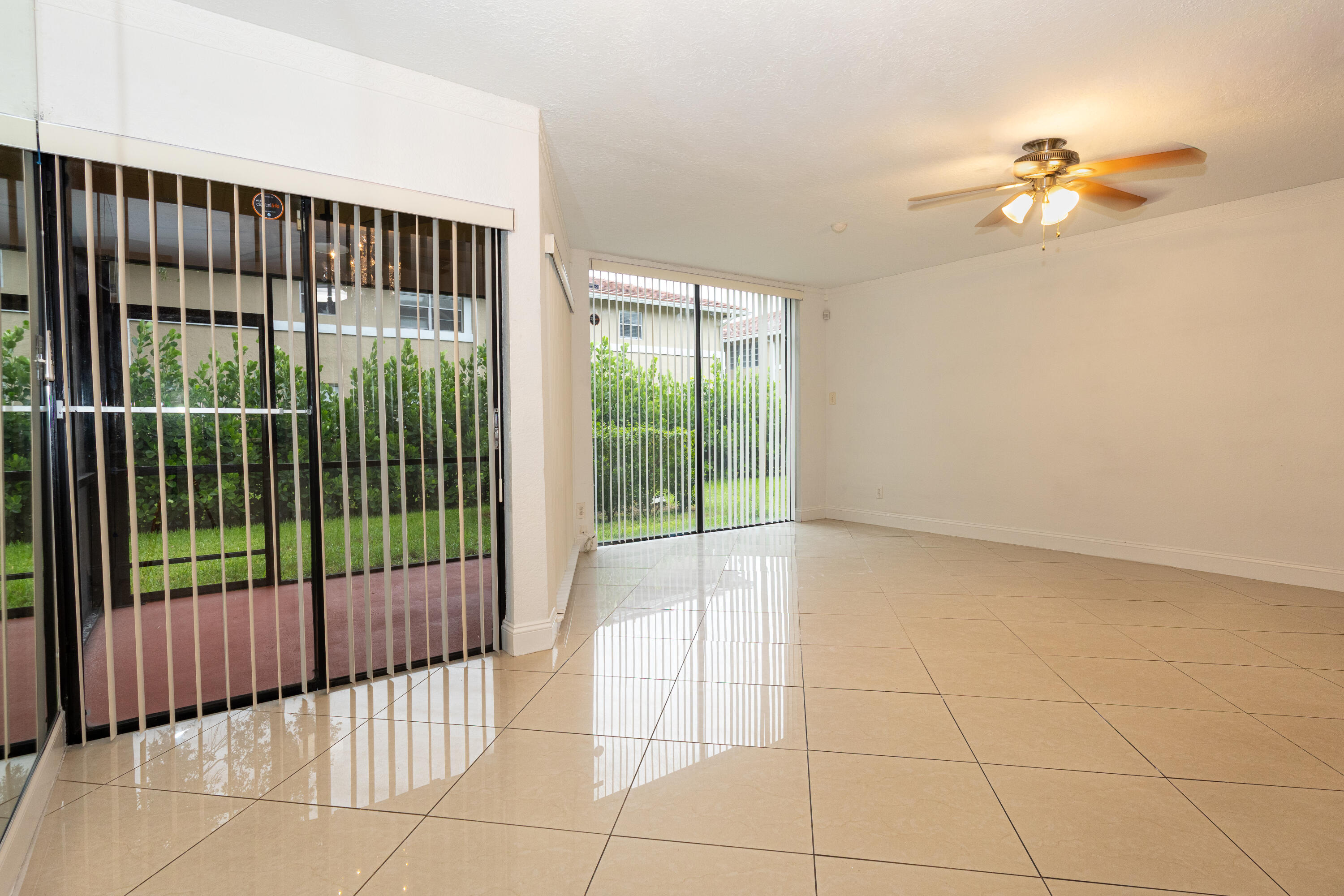 Expansive living area featuring large format tile flooring, a ceiling fan with integrated lighting, and multiple sliding glass doors leading to outdoor space Expansive living area featuring large format tile flooring, a ceiling fan with integrated lighting, and multiple sliding glass doors leading to outdoor space