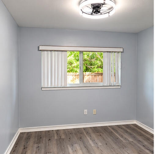 Room featuring neutral wall paint, wood-finish flooring, a ceiling-mounted light fixture, and a window with vertical blinds