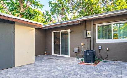 Paved patio featuring stone-finish pavers, sliding glass door, and exterior wall-mounted lighting