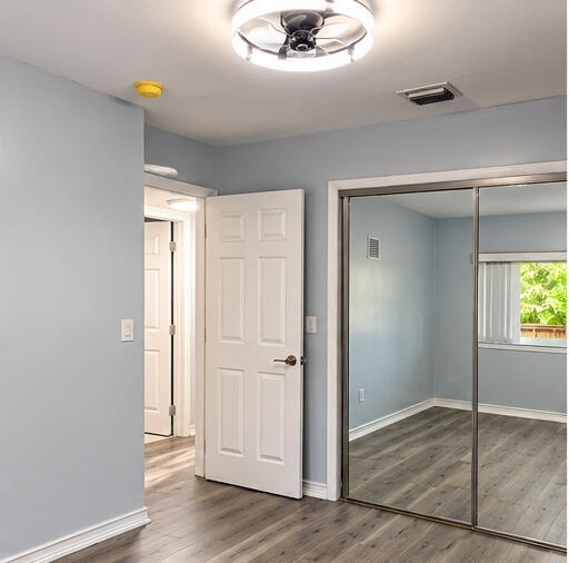 Wood-finish flooring, mirrored sliding closet doors, and modern integrated LED ceiling fan fixture