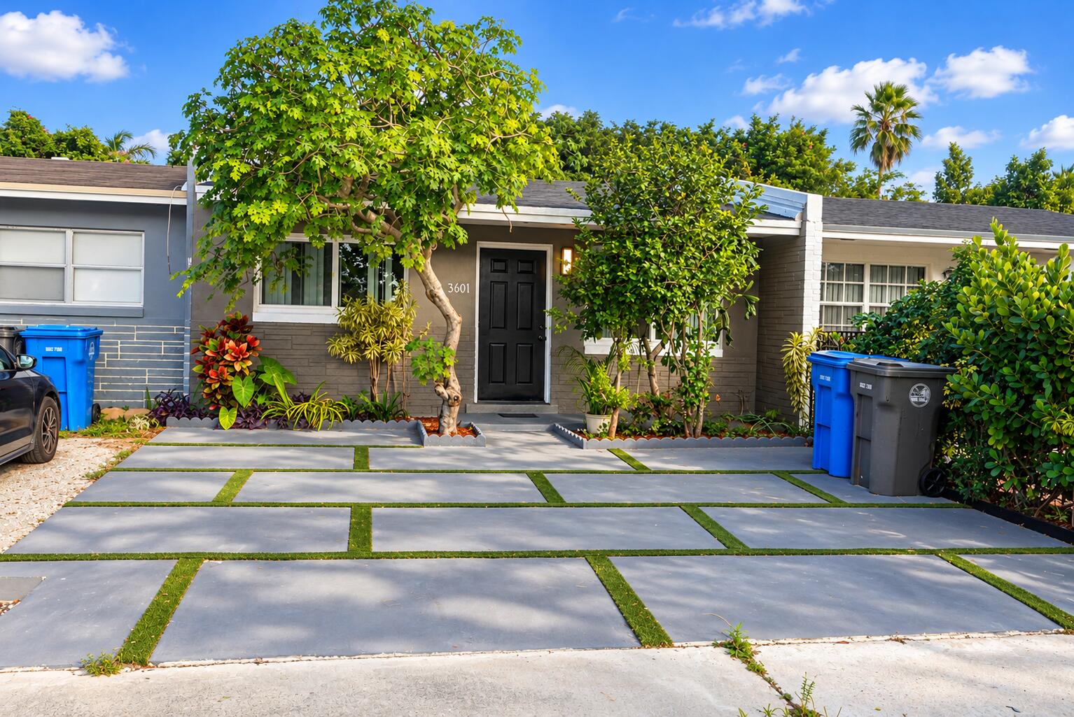 Grey brick exterior featuring a concrete paver driveway with integrated turf ribbons and mature landscaping