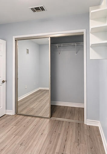 Sliding mirrored closet doors, wood-finish flooring, and built-in wall shelving