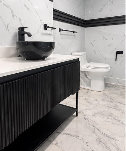 Black fluted vanity with a white countertop and a circular vessel sink, complemented by matte black hardware, wall-mounted faucet, and floor-to-ceiling stone-patterned wall tiling