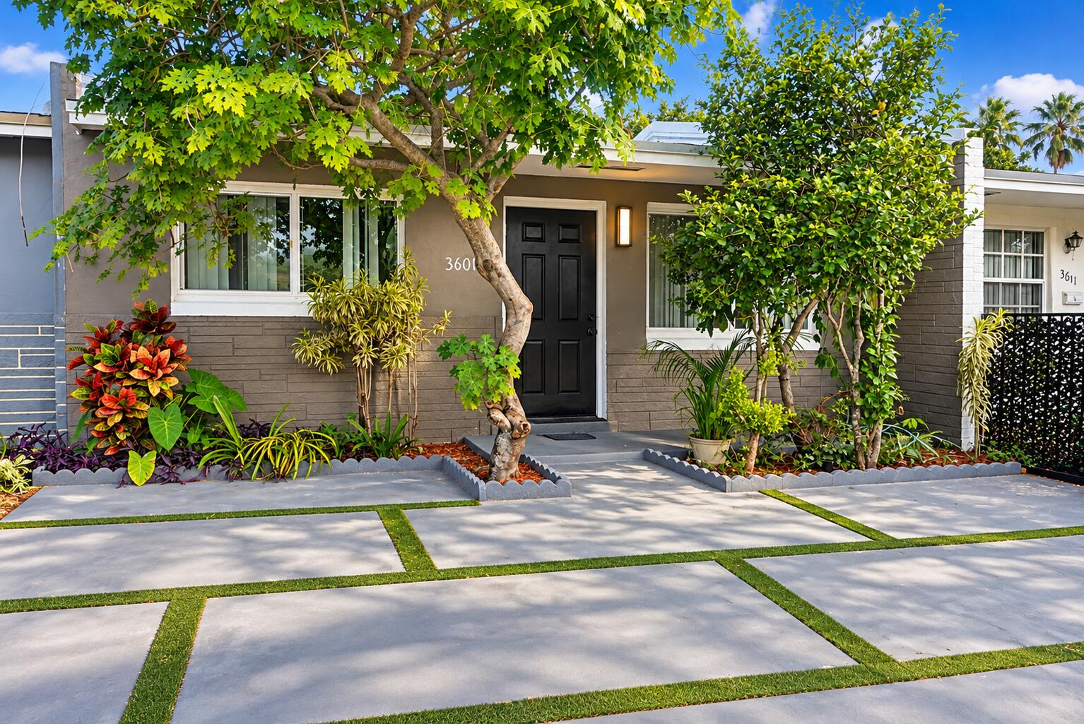 Exterior facade featuring concrete paver driveway with turf accents, mature landscaping.