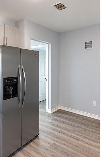 Stainless steel side-by-side refrigerator, white shaker-style cabinetry, and wood-finish flooring