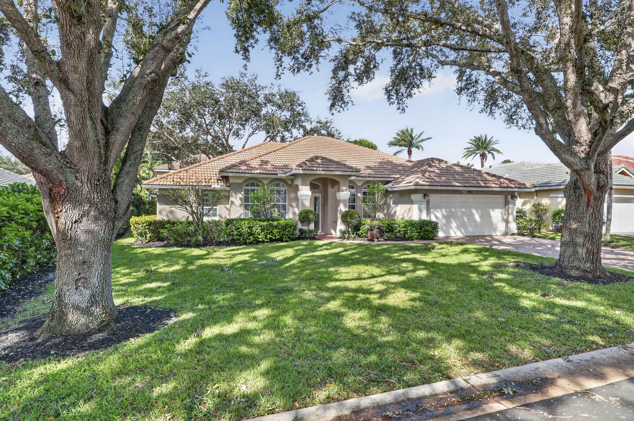 Single-story residence featuring a tile roof, arched entryway, multi-paned windows, a two-car garage, and mature landscape Single-story residence featuring a tile roof, arched entryway, multi-paned windows, a two-car garage, and mature landscape