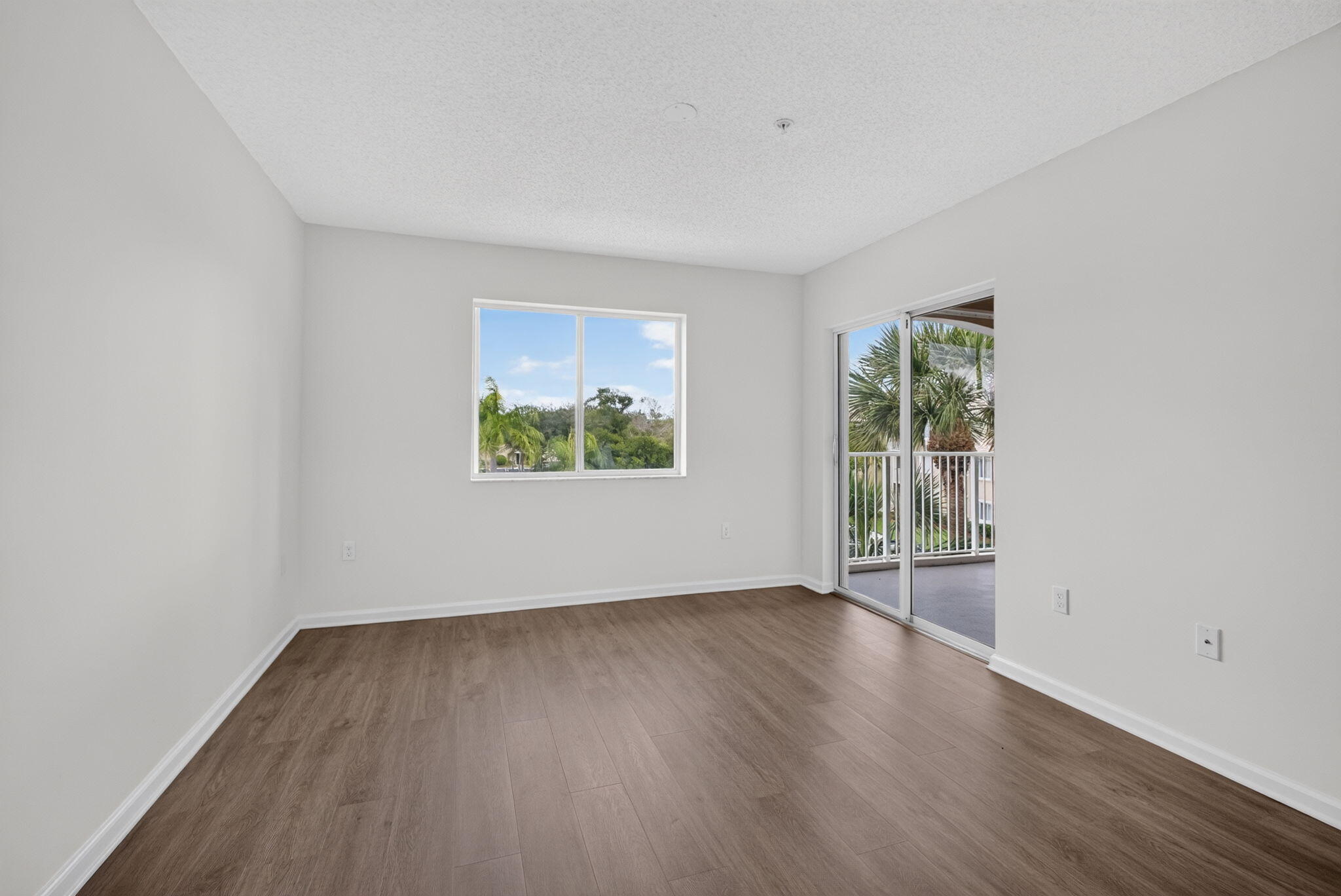 Interior space featuring vinyl plank flooring, neutral wall tones, a large dual-pane window, and a sliding glass door providing access to covered balcony