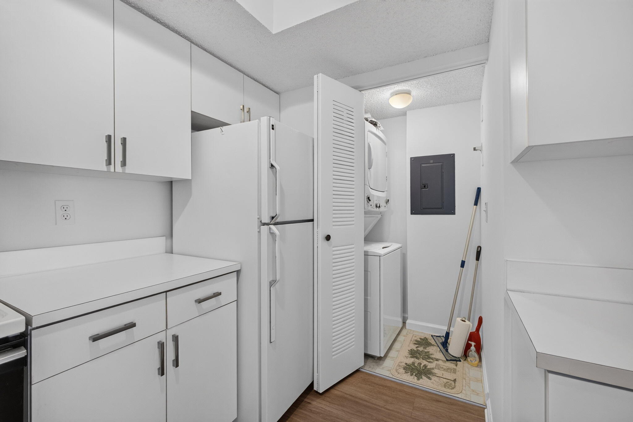 Kitchen featuring white cabinetry, solid-surface countertops, full-size refrigerator, and louvered-door closet containing a stacked laundry unit