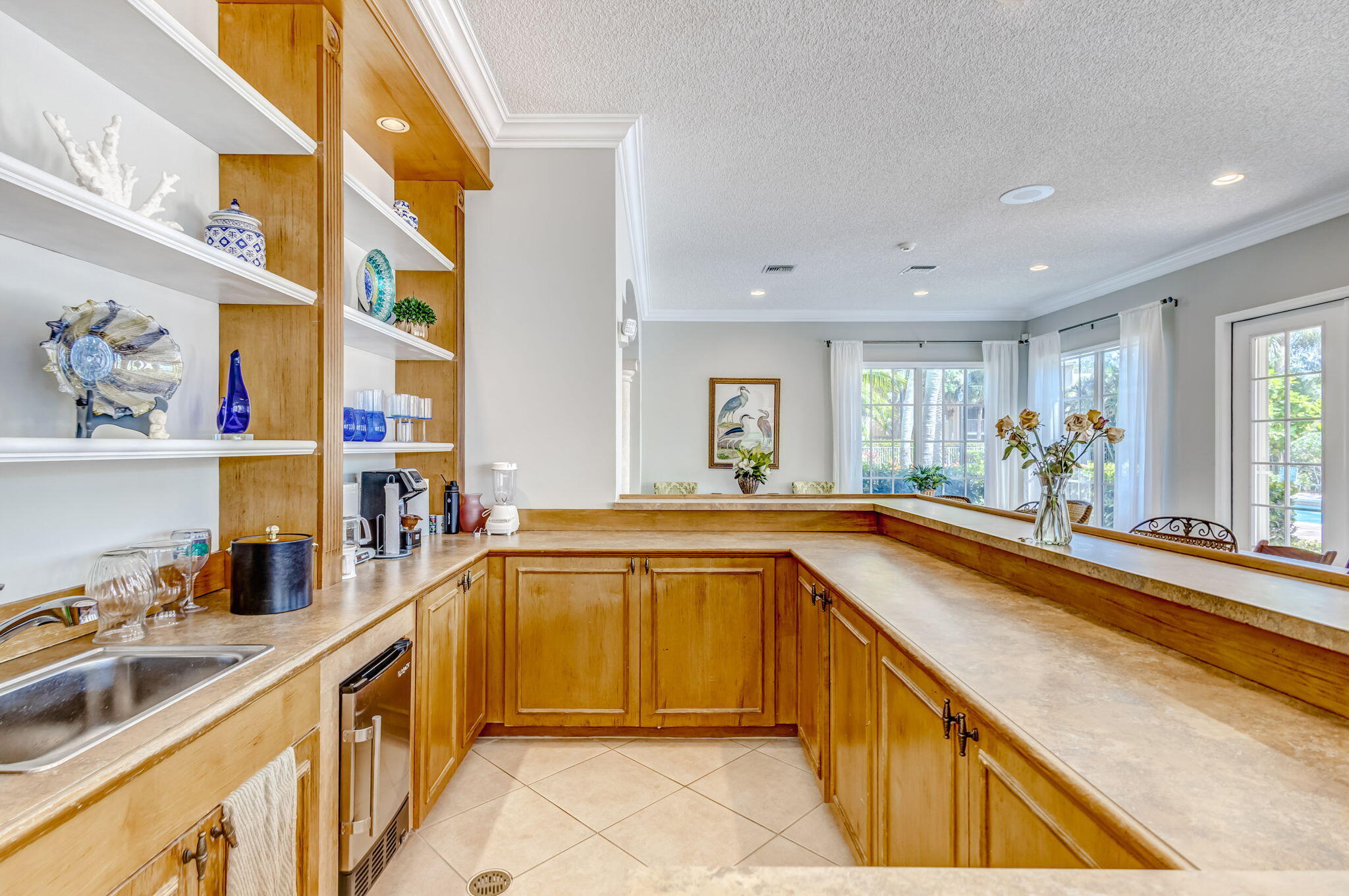 Custom built-in cabinetry with integrated open shelving, stone-finish countertops, stainless steel under-mount sink, tile flooring, and recessed lighting