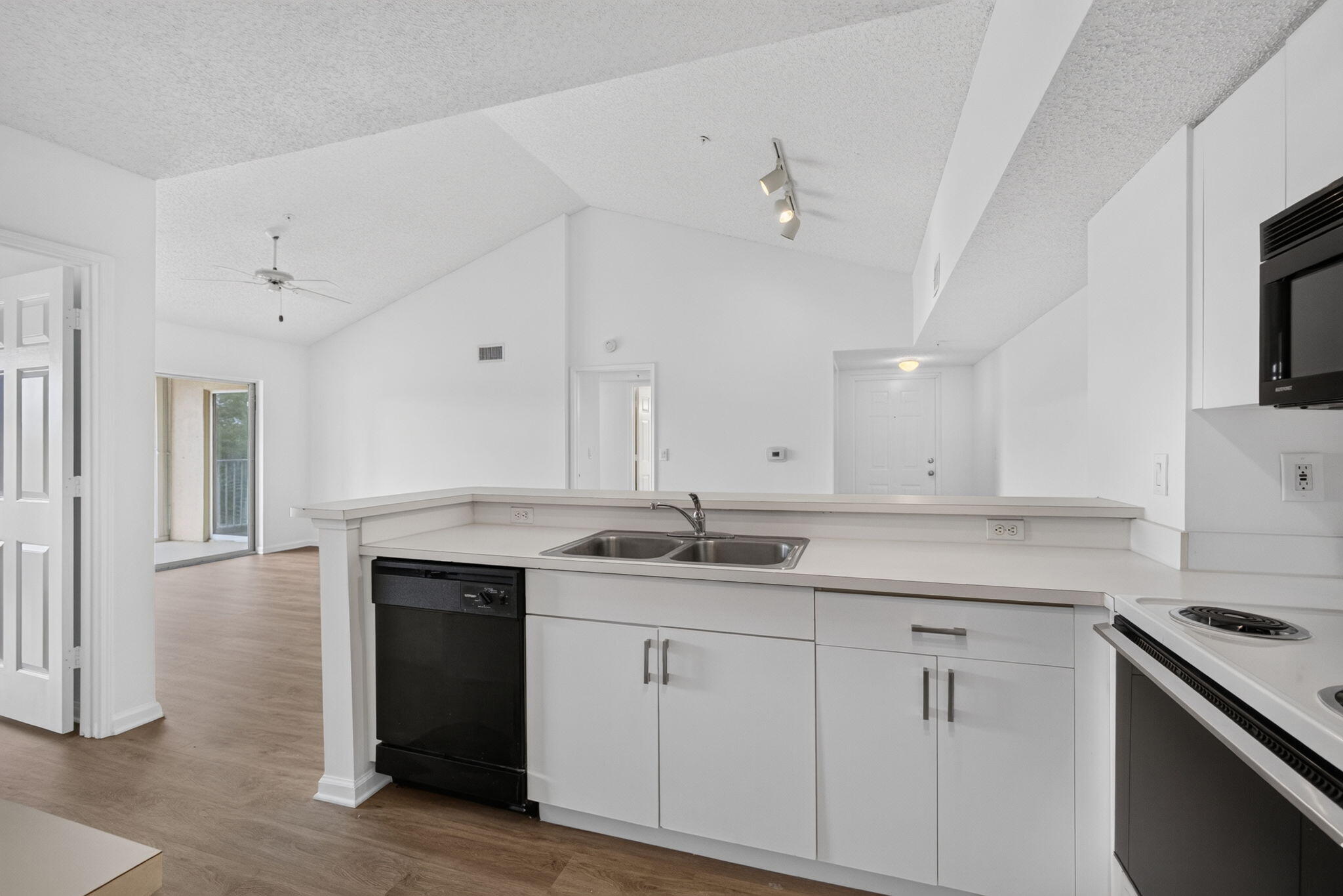 Kitchen featuring white cabinetry, solid-surface countertops, dual-basin stainless steel sink, and black built-in appliances under a vaulted ceiling